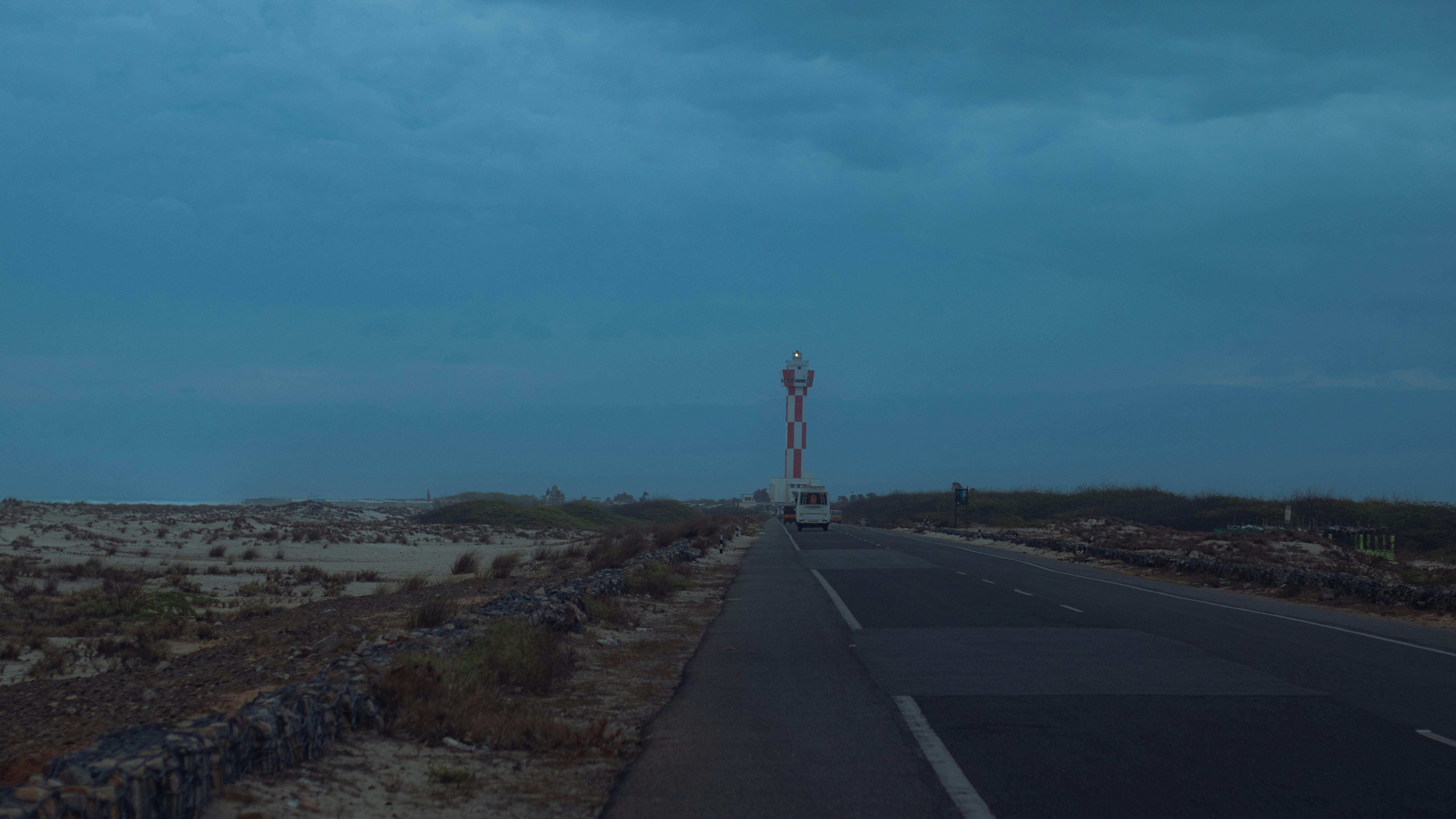 Road leading to a tall tower under a cloudy sky