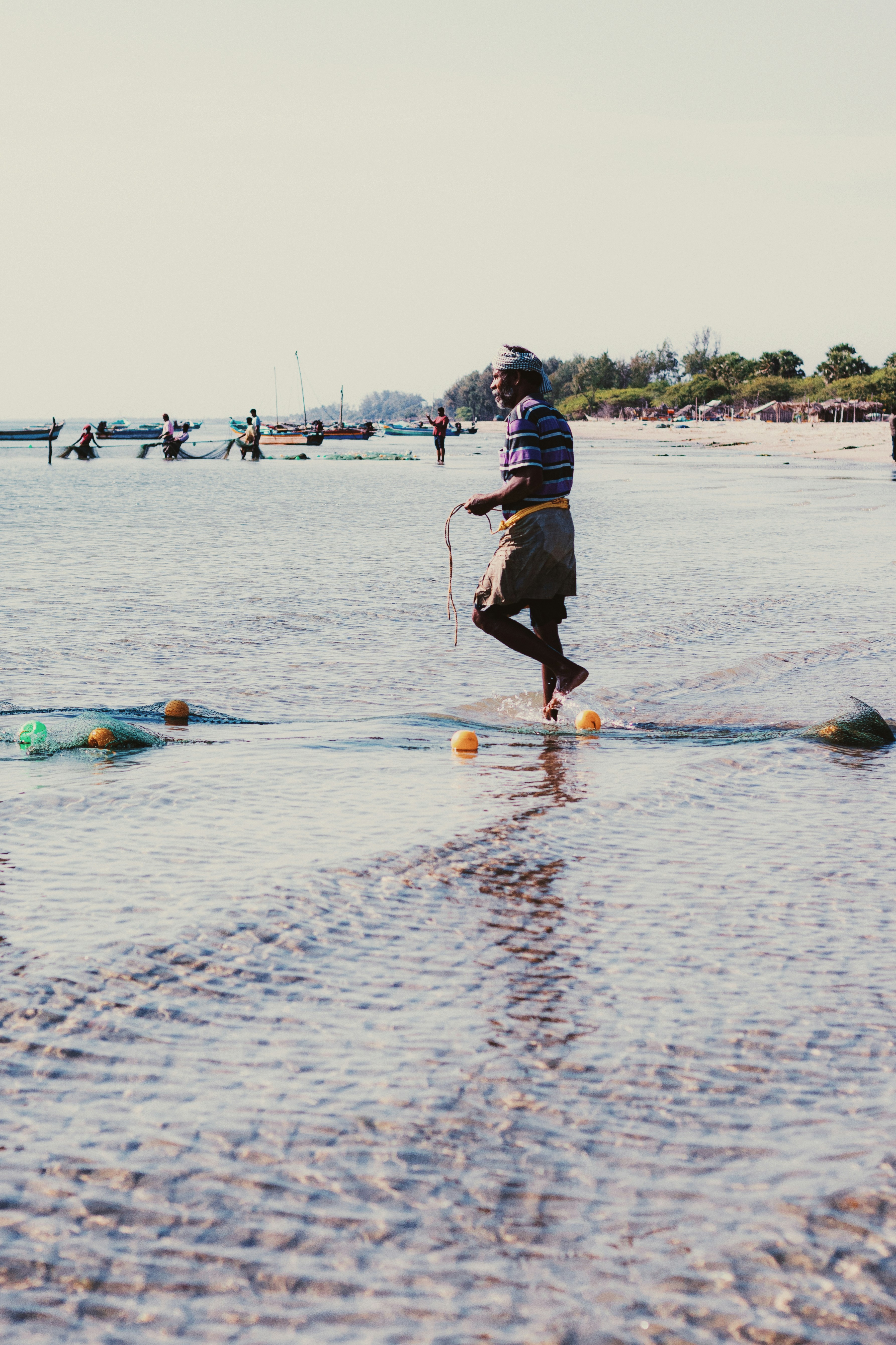 Fisherman pulls fishing net through shallow ocean water.