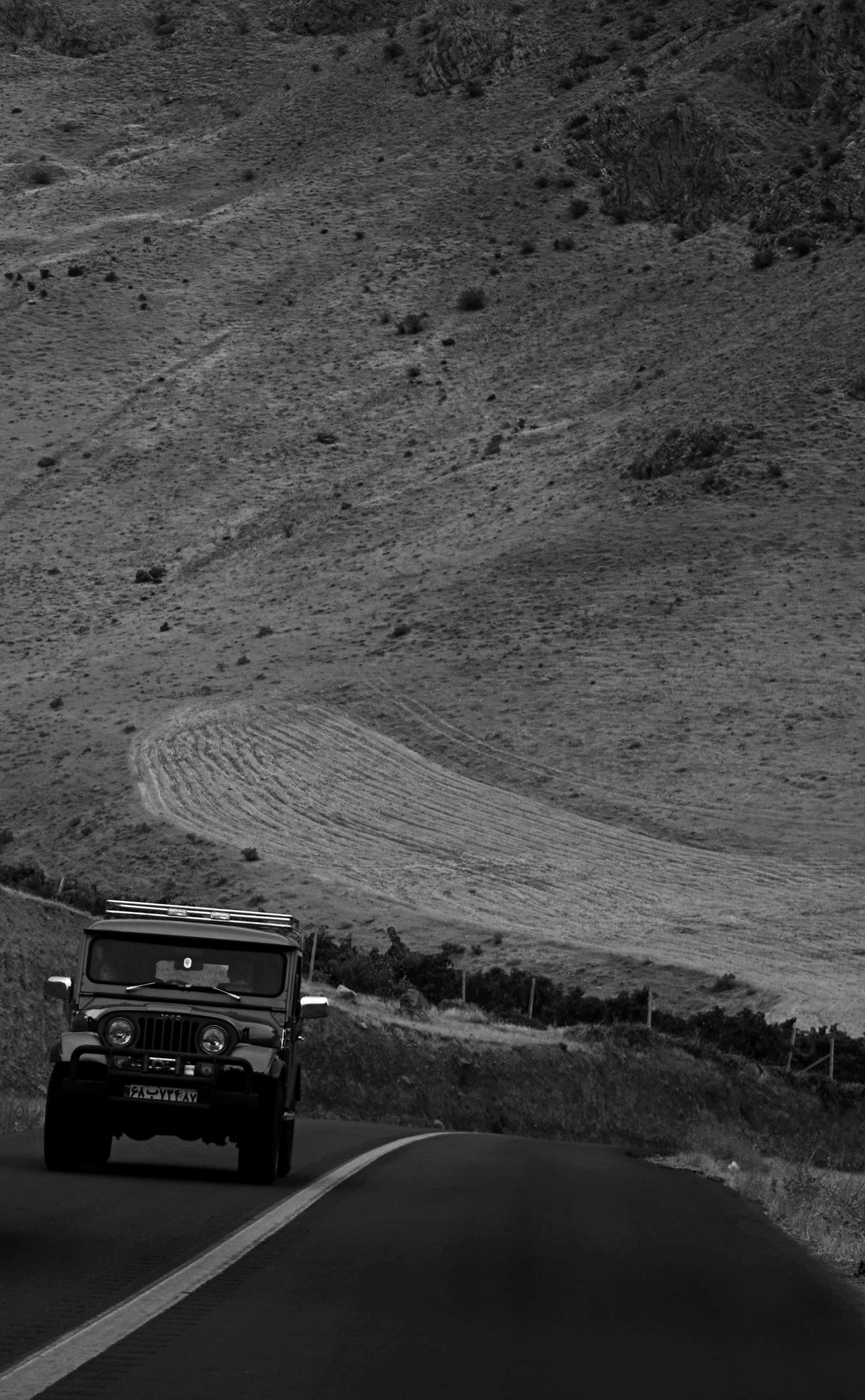 A vehicle drives on a winding road through hills.
