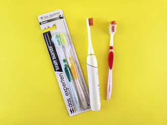 Two toothbrushes and packaging on yellow background