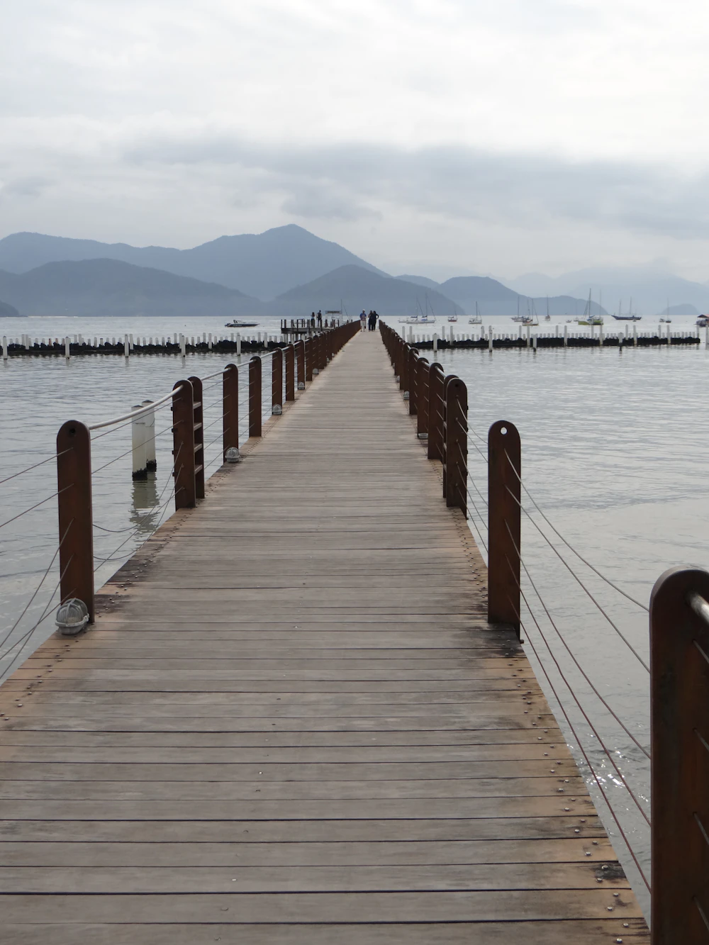 Píer sobre a água calma, com montanhas ao fundo, em Ubatuba