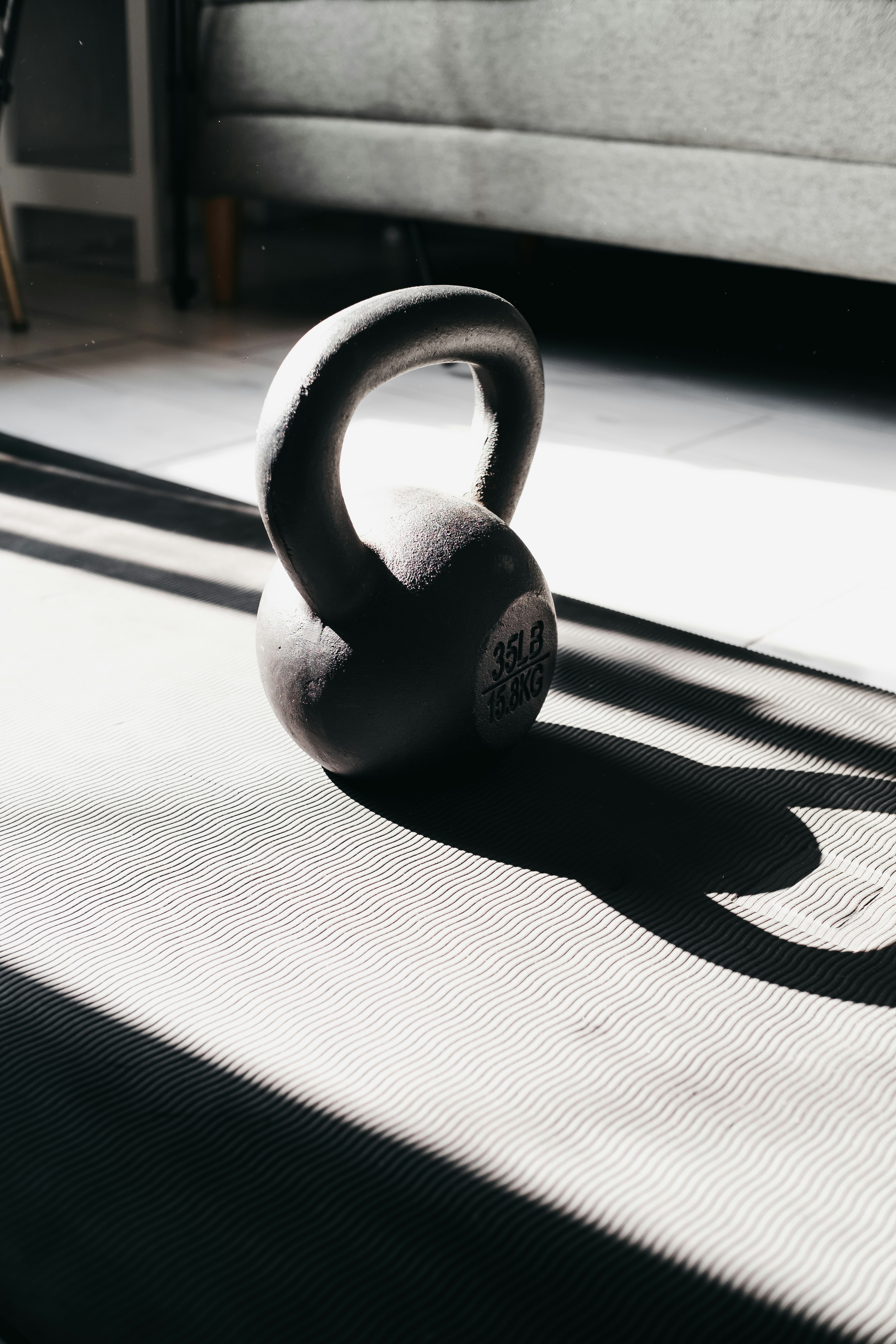 A kettlebell rests on a yoga mat in sunlight.