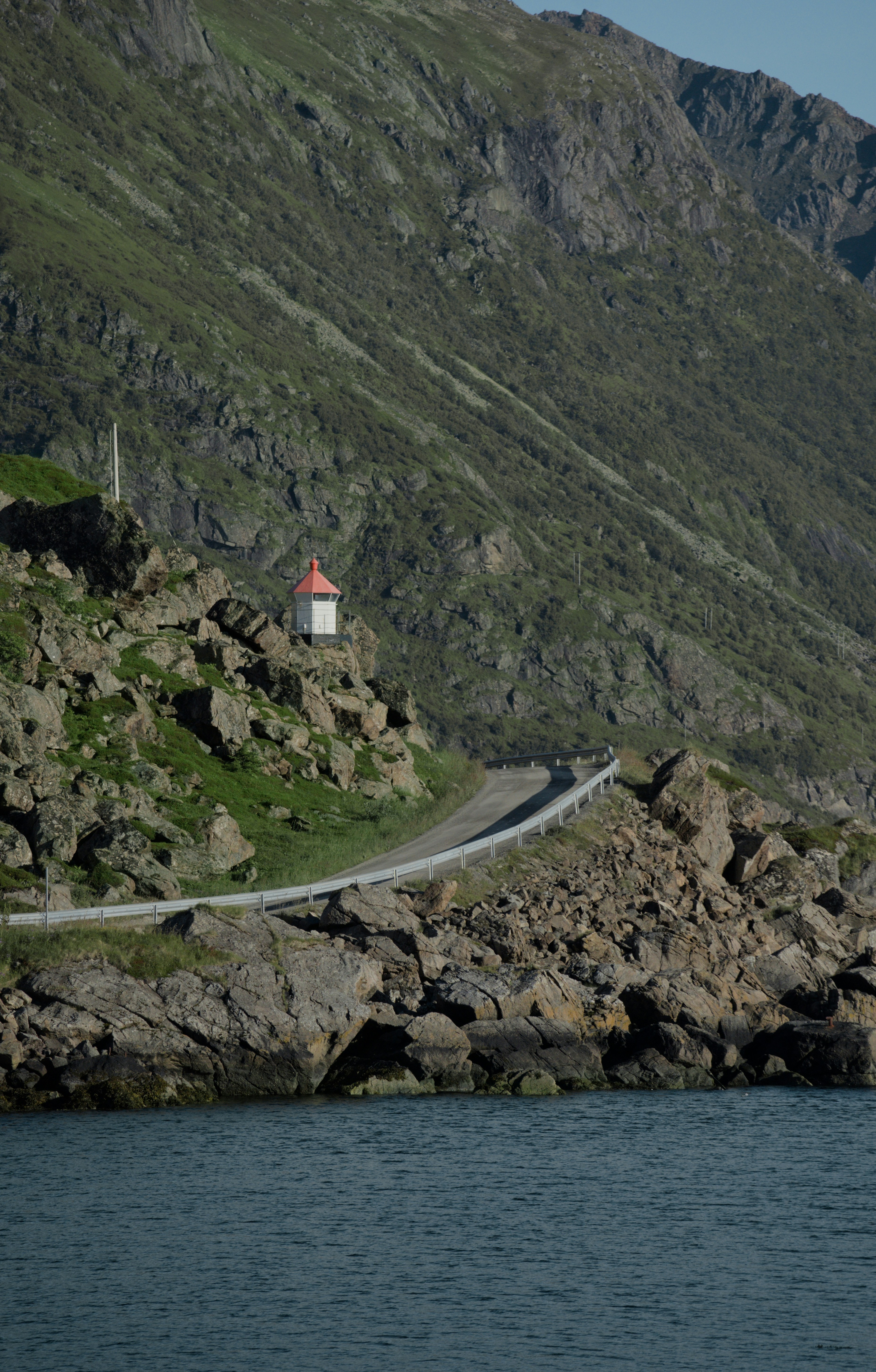 Coastal road leads to lighthouse and small building.