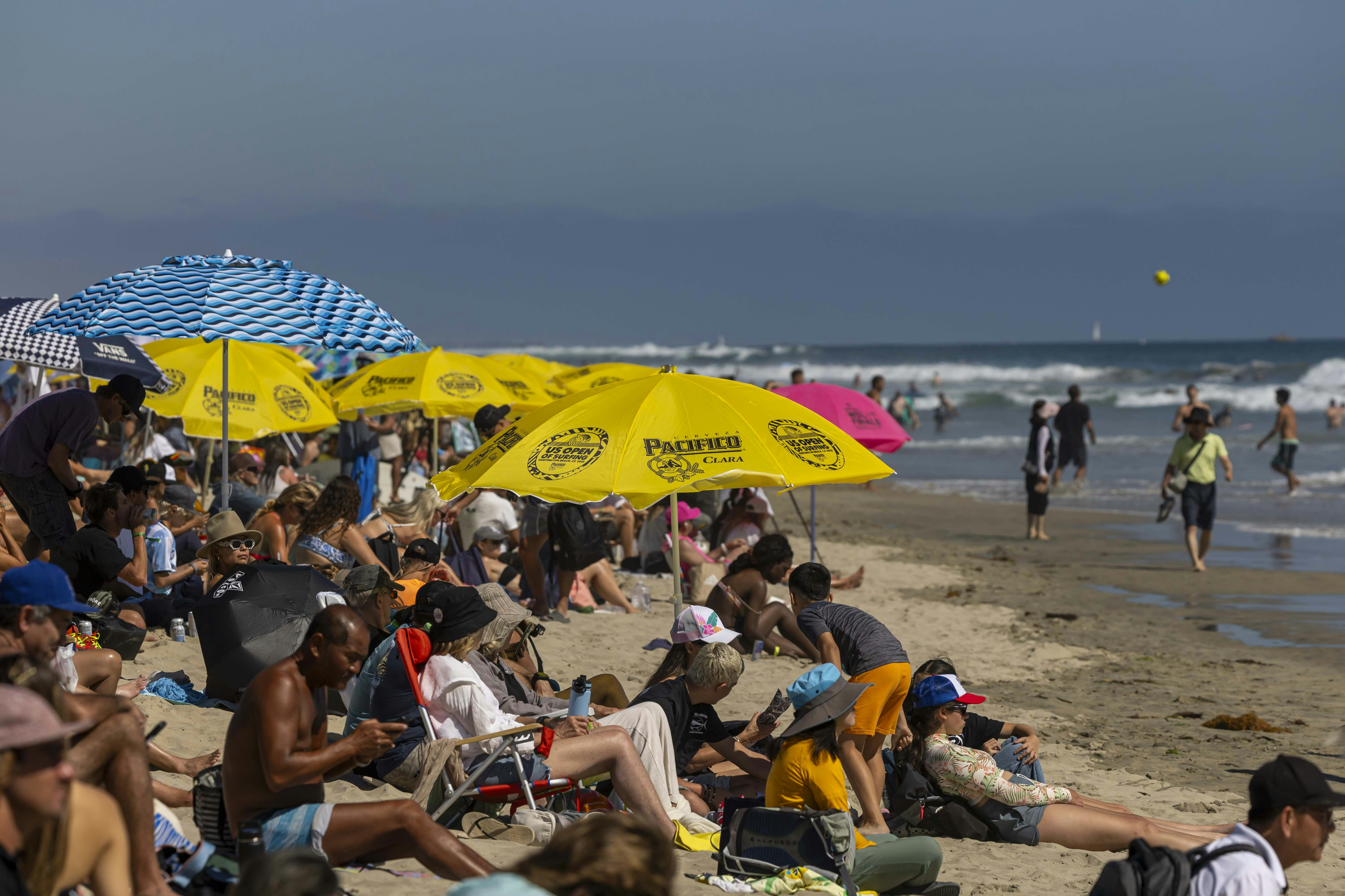People relax on a crowded beach with colorful umbrellas.