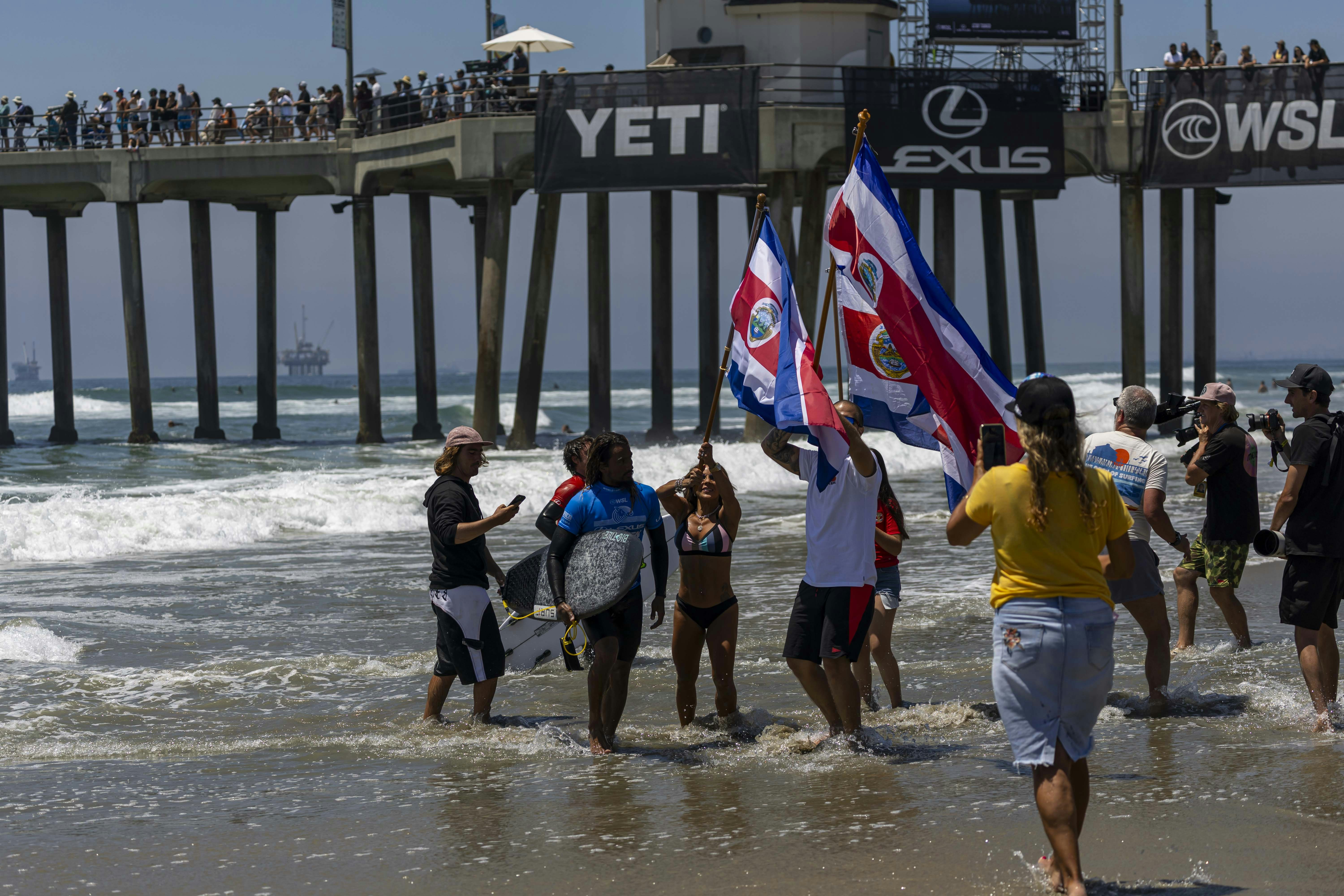 Des personnes avec des drapeaux marchent sur une plage près d’une jetée