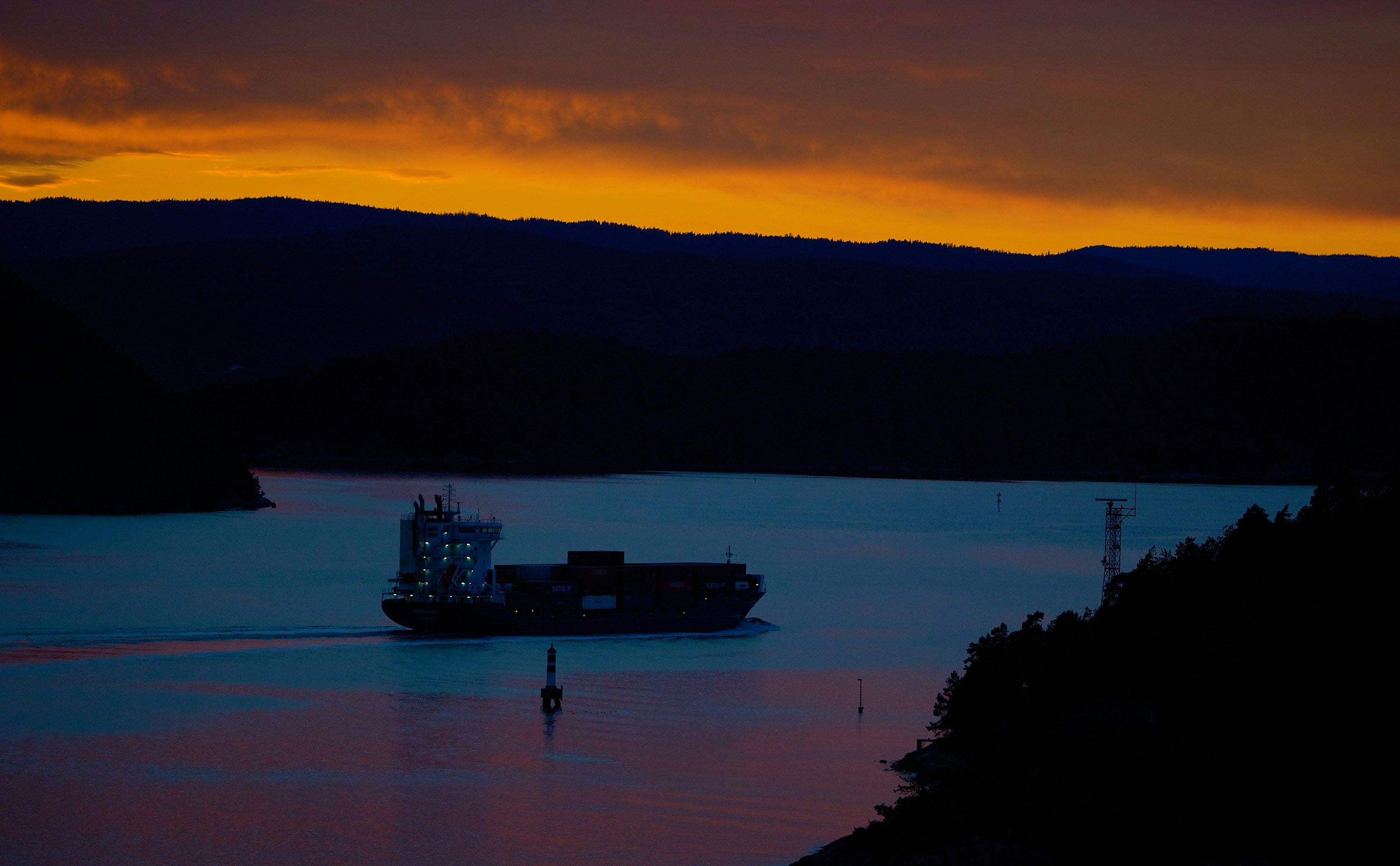 Cargo ship sailing on water at sunset