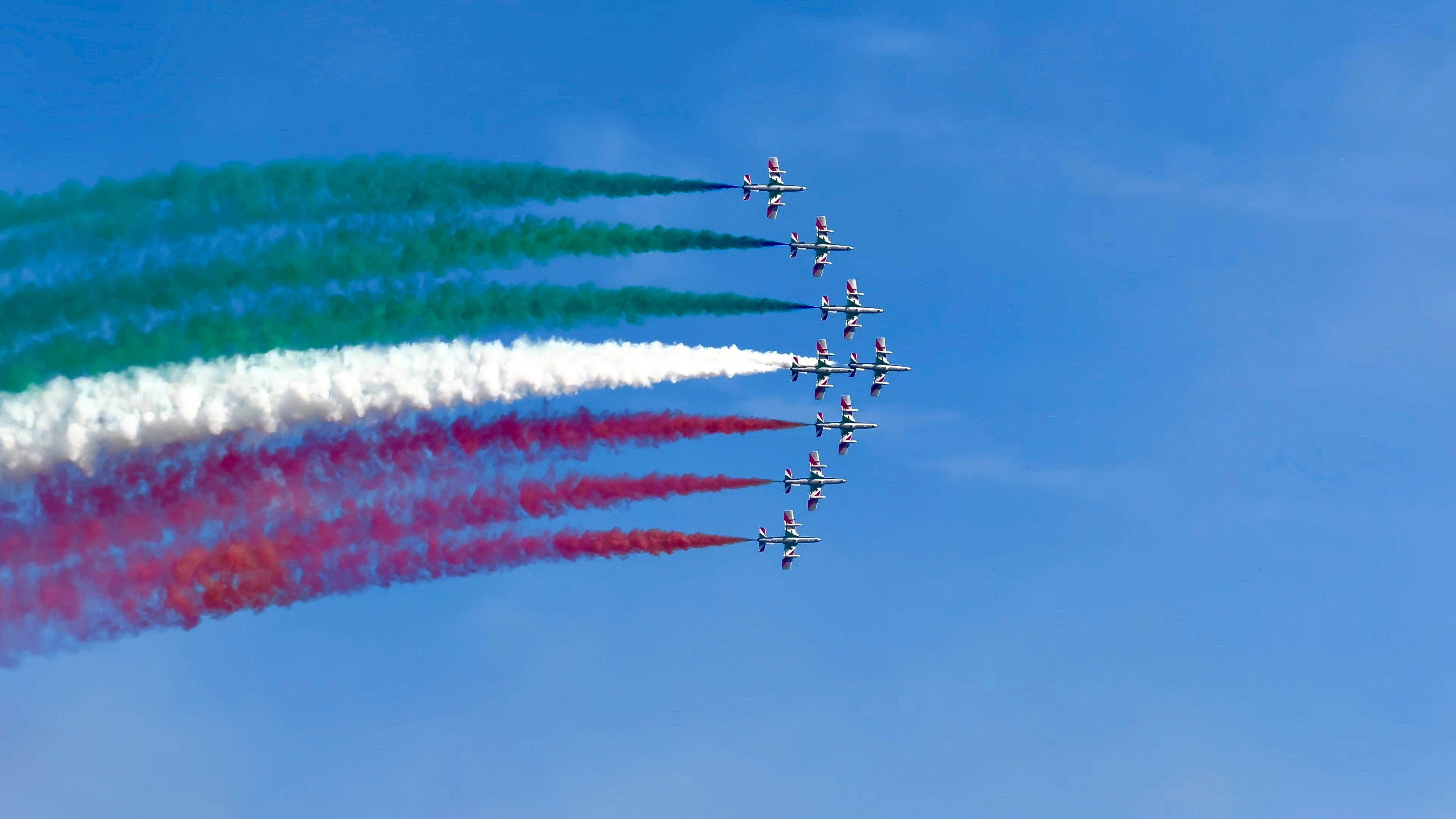 Airplanes trail colorful smoke across a blue sky