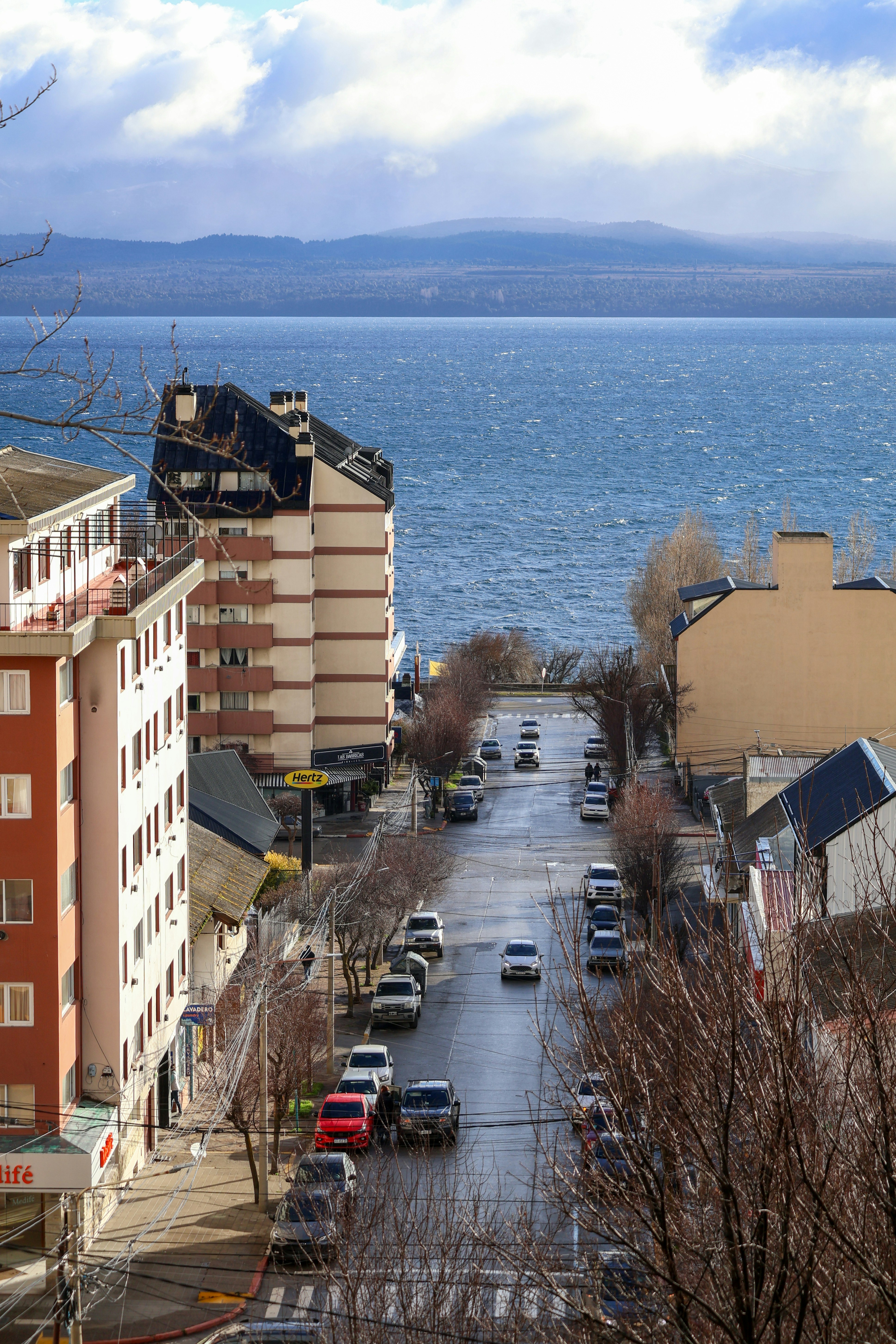City street leads to a calm blue lake under clouds