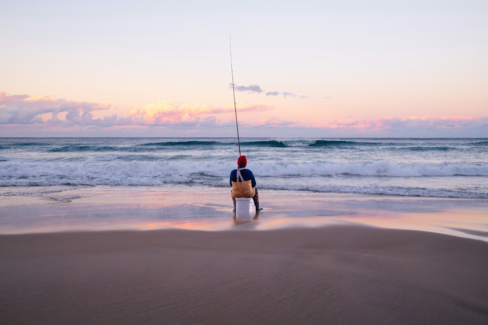 Angler sitting on a cooler surf fishing at sunrise on the beach
