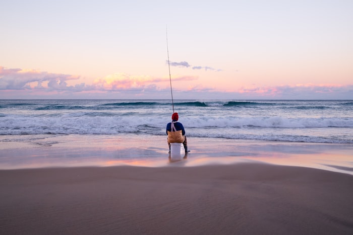 Angler sitting on a cooler surf fishing at sunrise on the beach