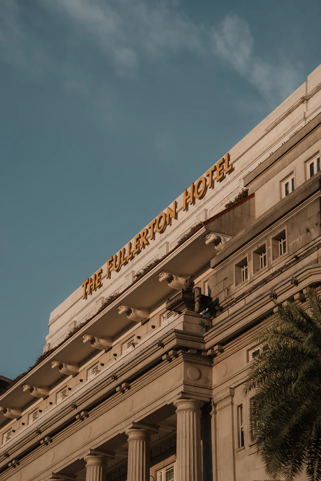 Low-angle view of The Fullerton Hotel's neoclassical facade with its gold 'THE FULLERTON HOTEL' signage against the sky.