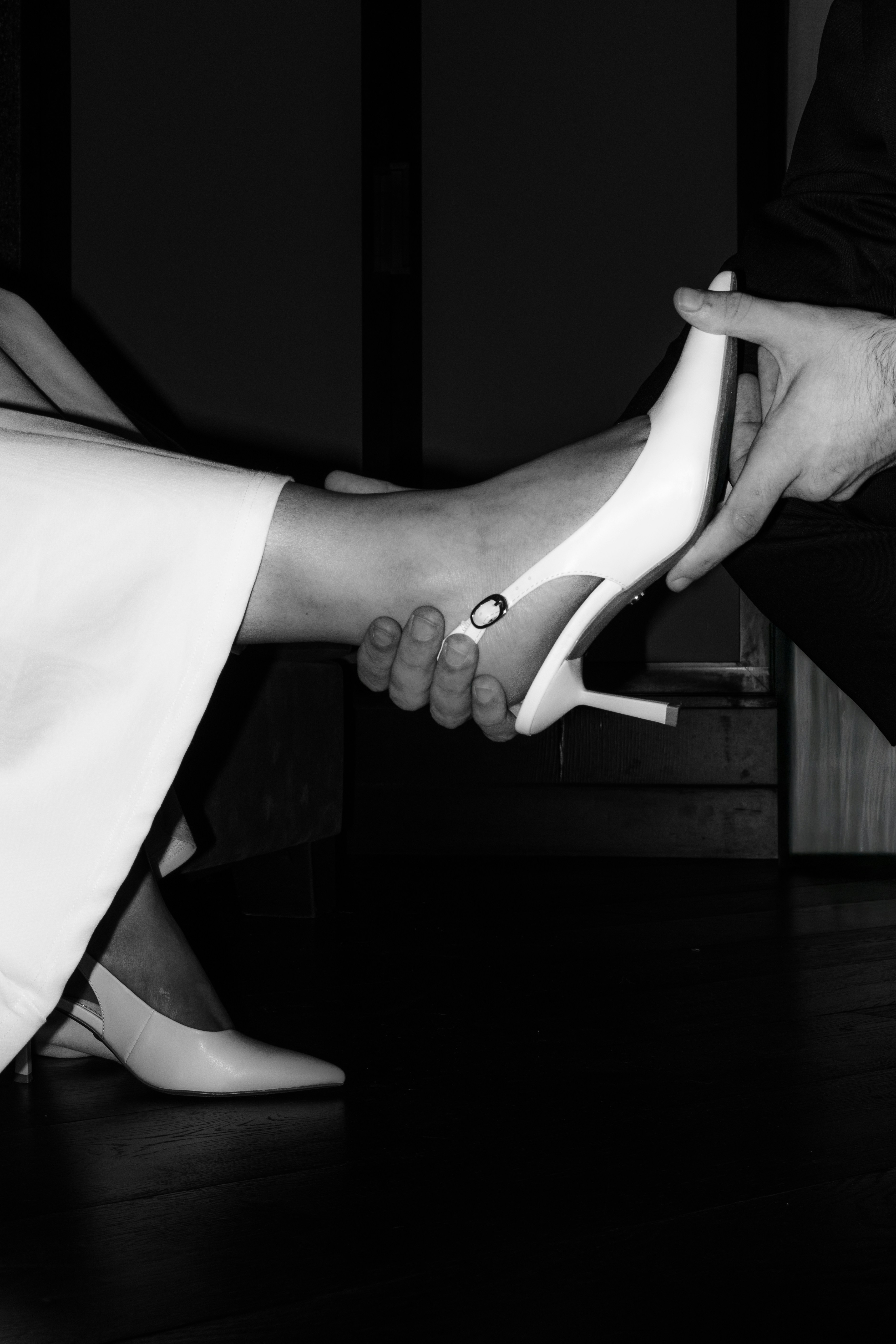 A hand helps a woman put on a white high heel.