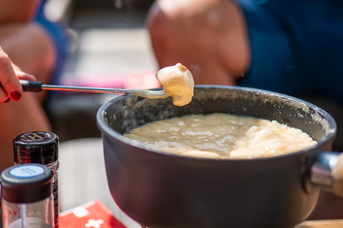 Fourchette à fondue soulevant un morceau de pain nappé de fromage au-dessus du caquelon