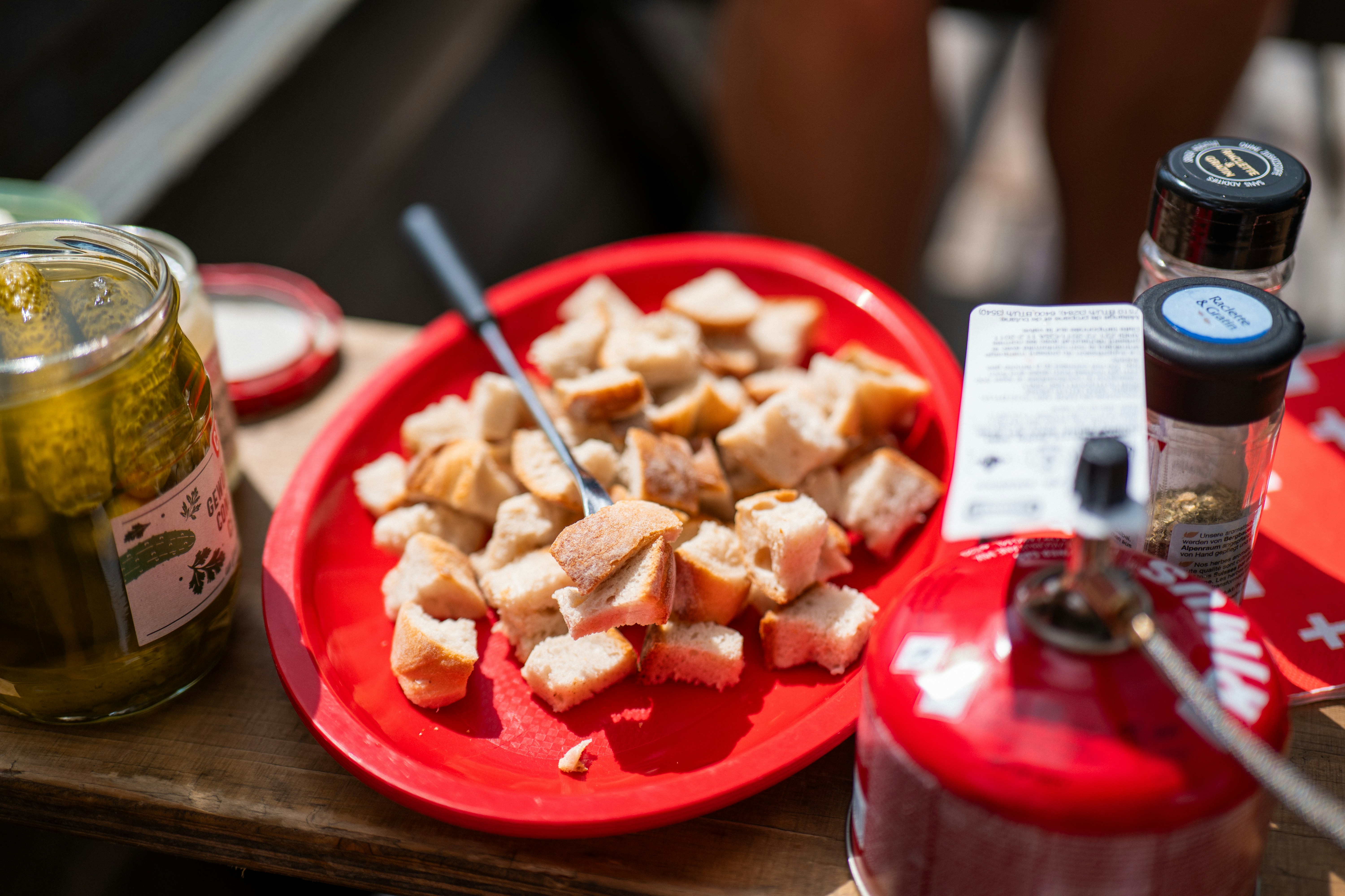 Croutons on a red plate with pickles and seasonings.