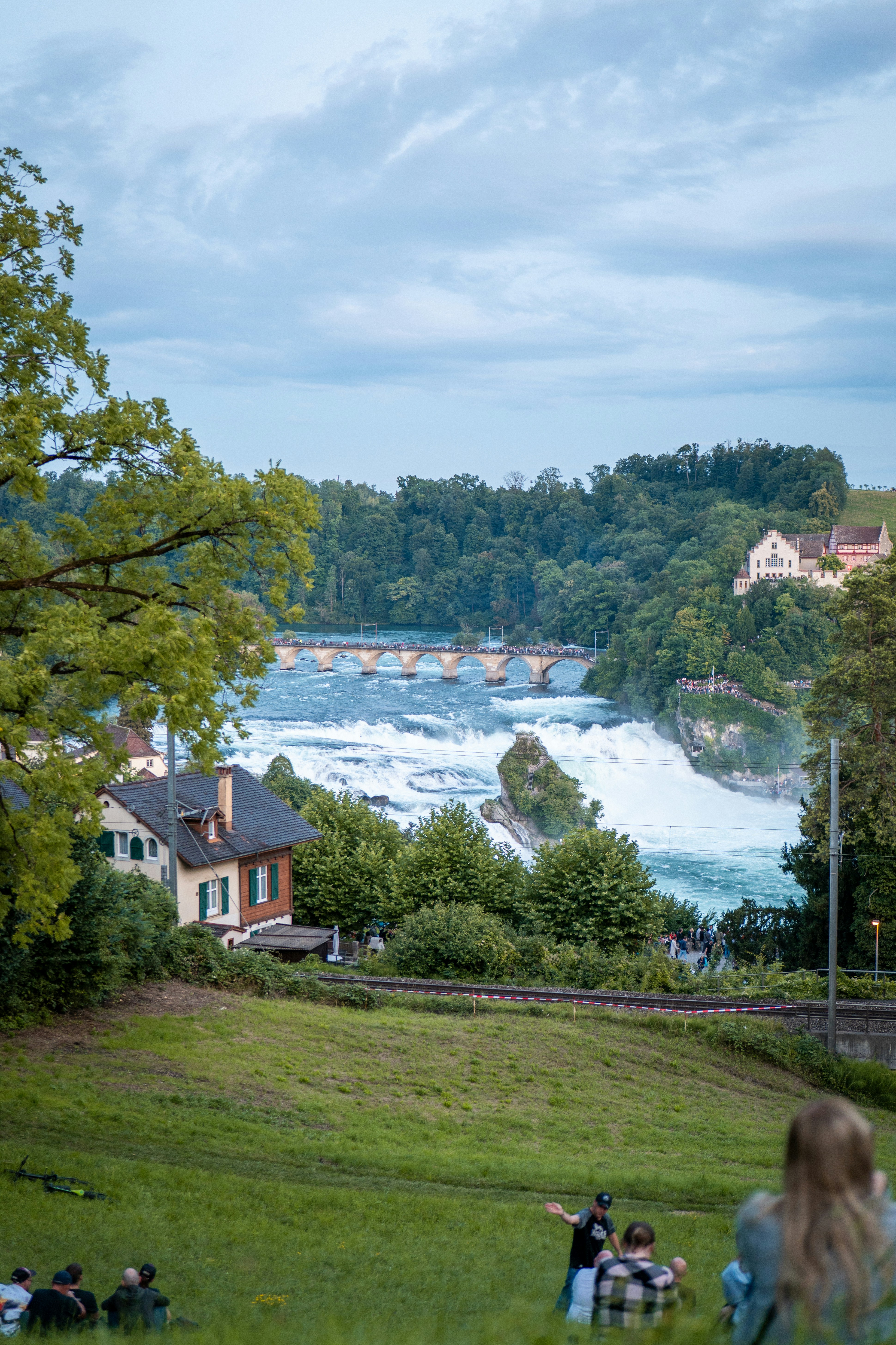 People relax on a grassy hill overlooking a powerful waterfall.