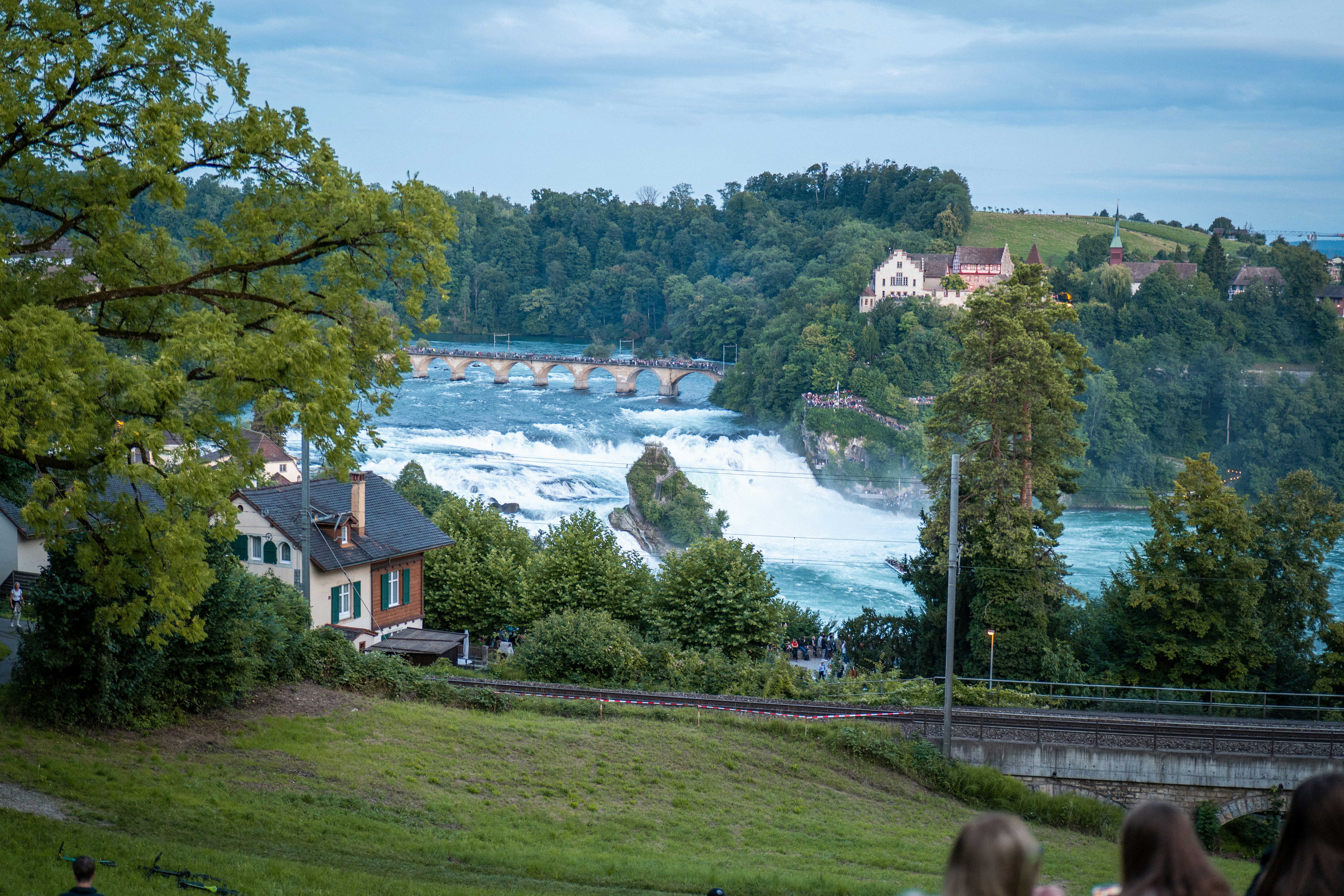 Powerful waterfall with lush green trees and buildings.