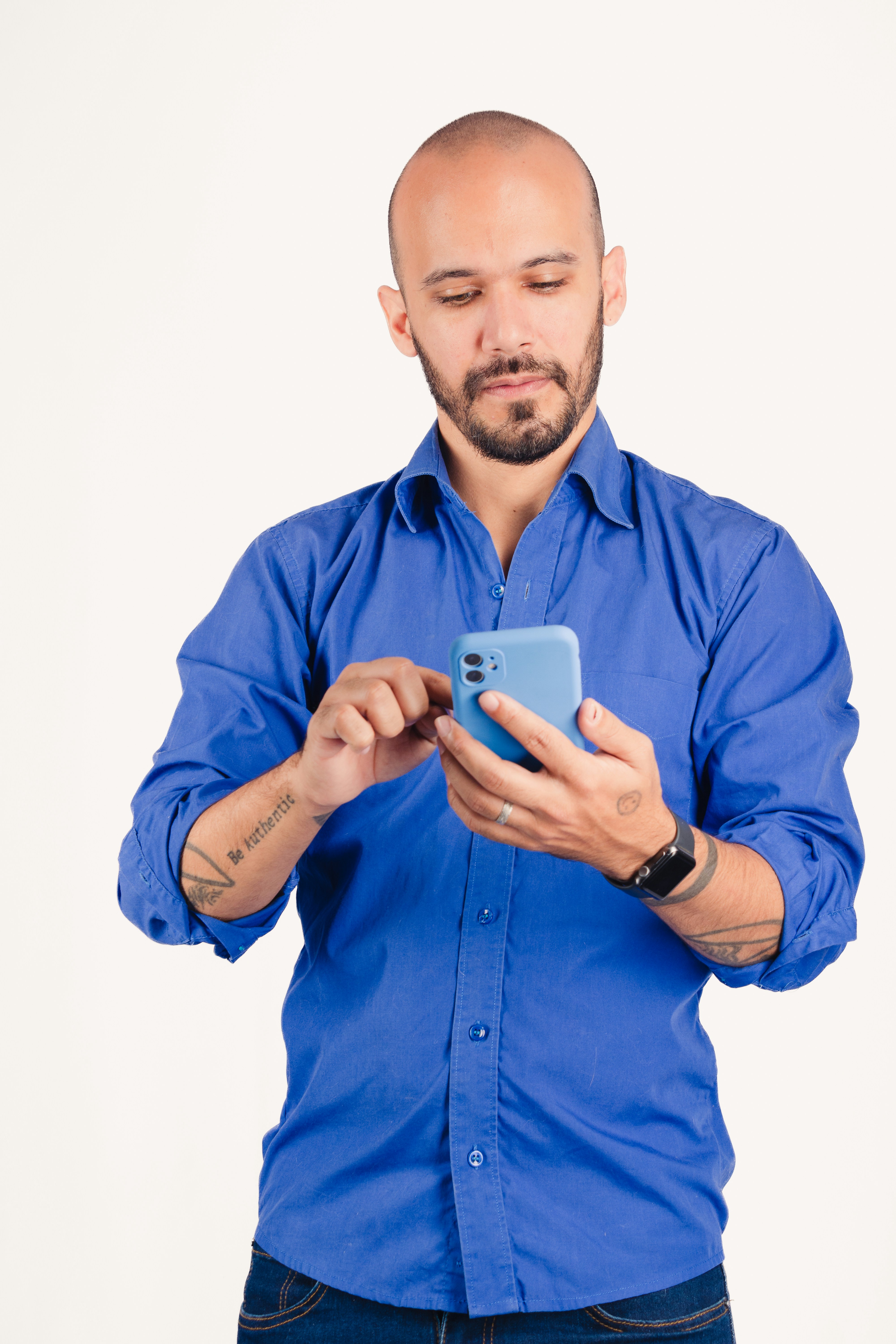 Bald man in blue shirt using smartphone on white background