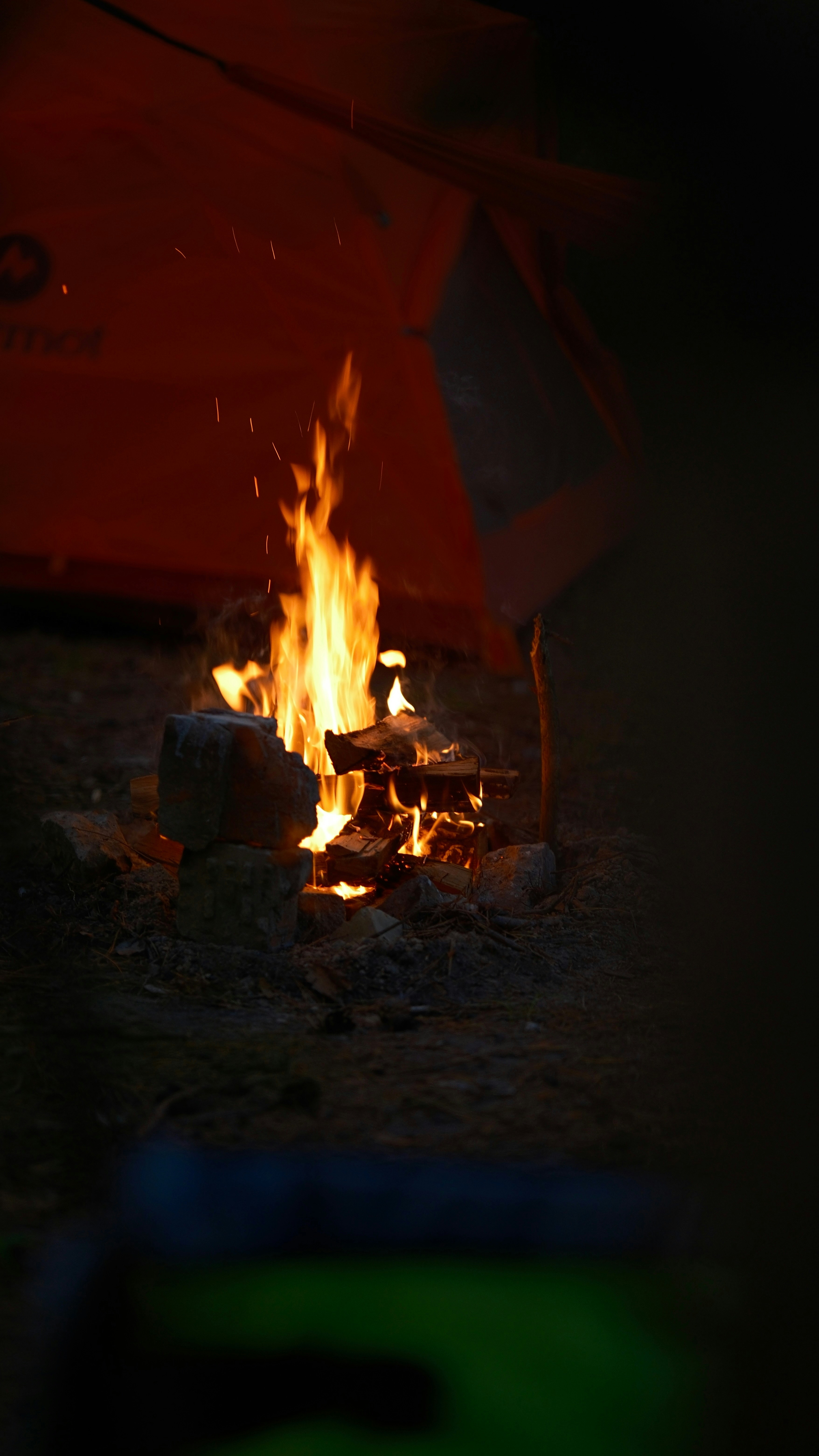 Campfire burning brightly next to an orange tent at night