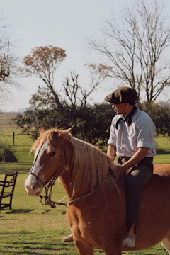 Man in flat cap riding a brown horse outdoors