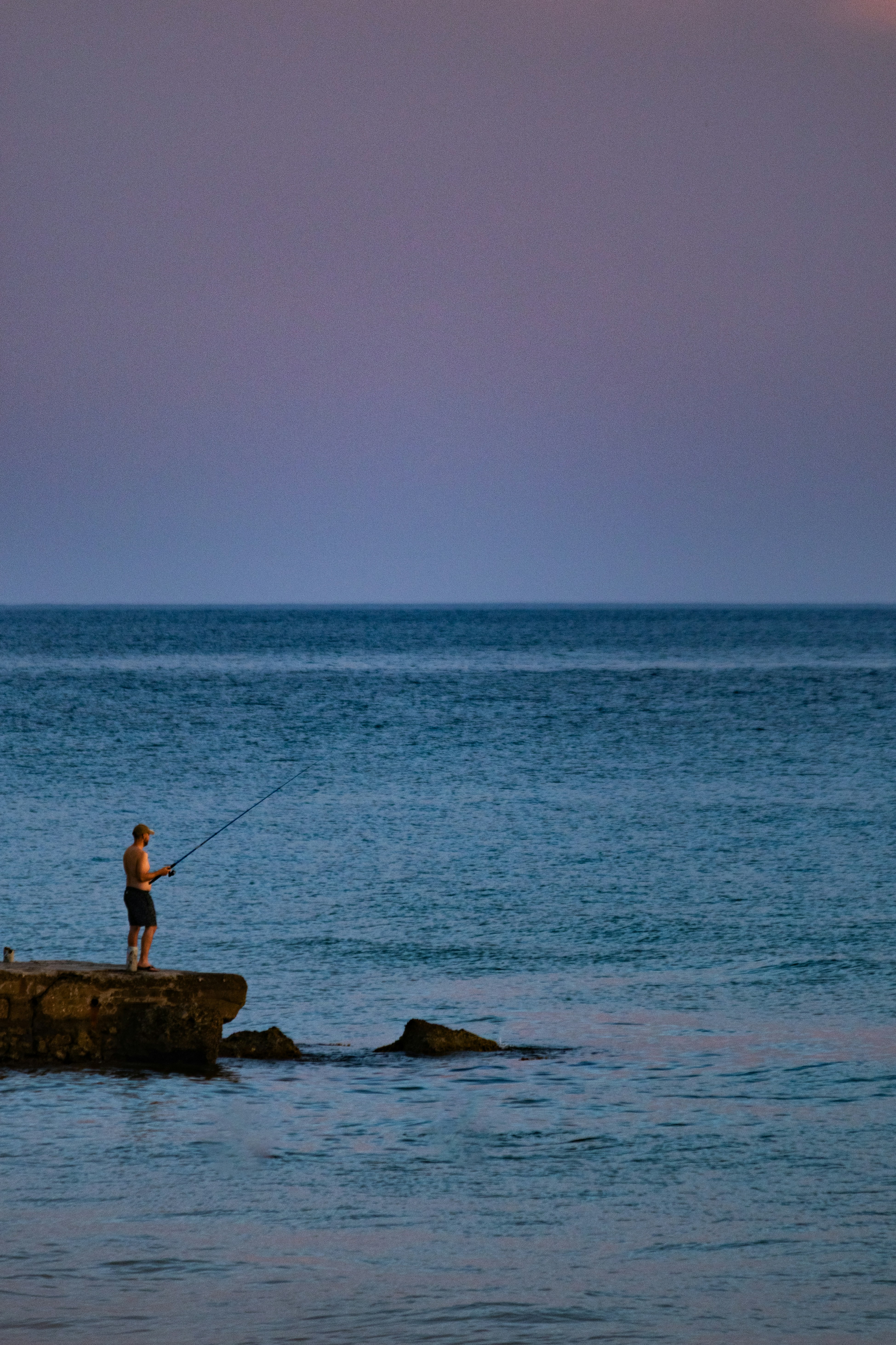 Man fishing from a rocky shore at sunset