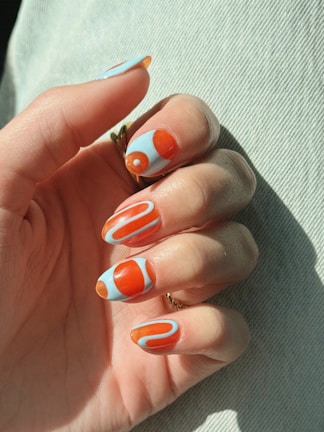 Hand with light blue and orange abstract patterned nails