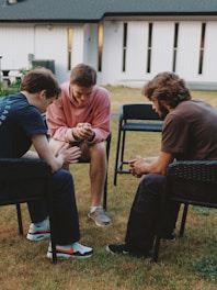 Three young men sitting in a circle praying.