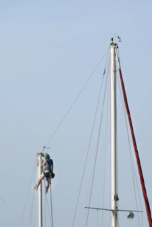 Sailors working on a tall sailboat mast