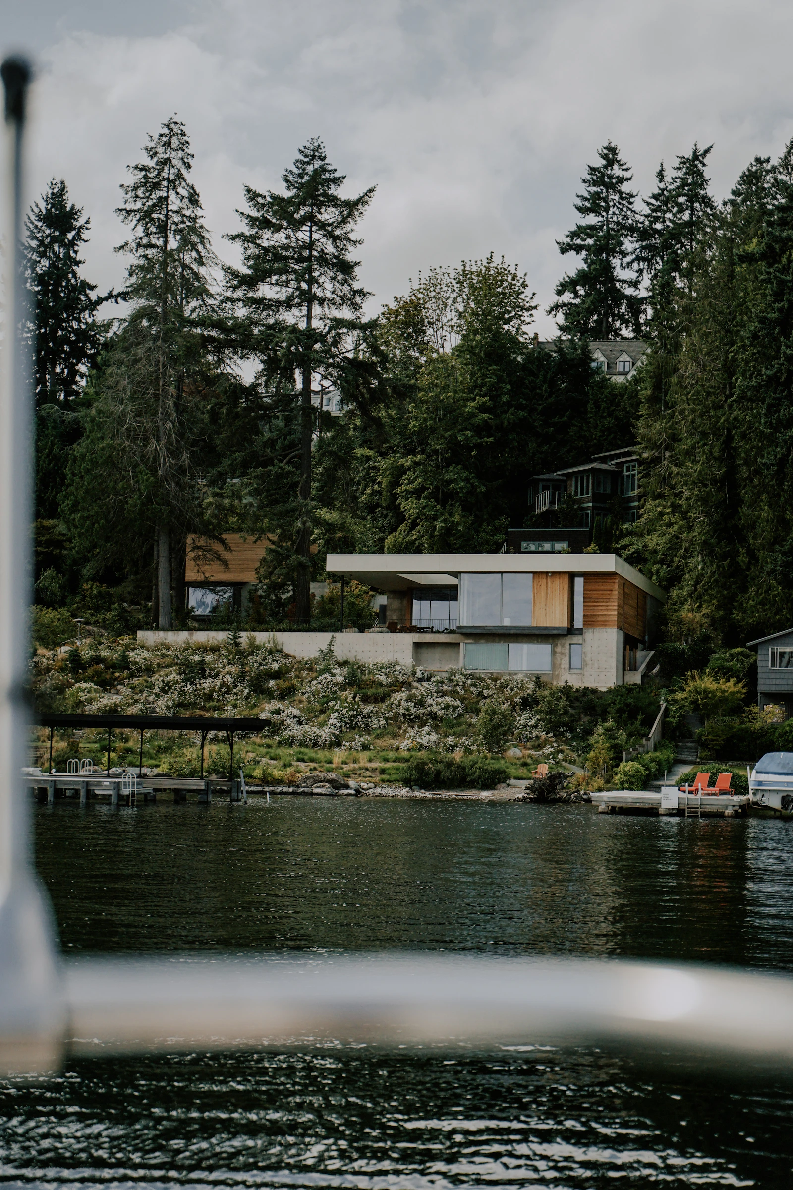 Modern flat-roofed lakefront house with floor-to-ceiling windows nestled among tall evergreens above a private dock