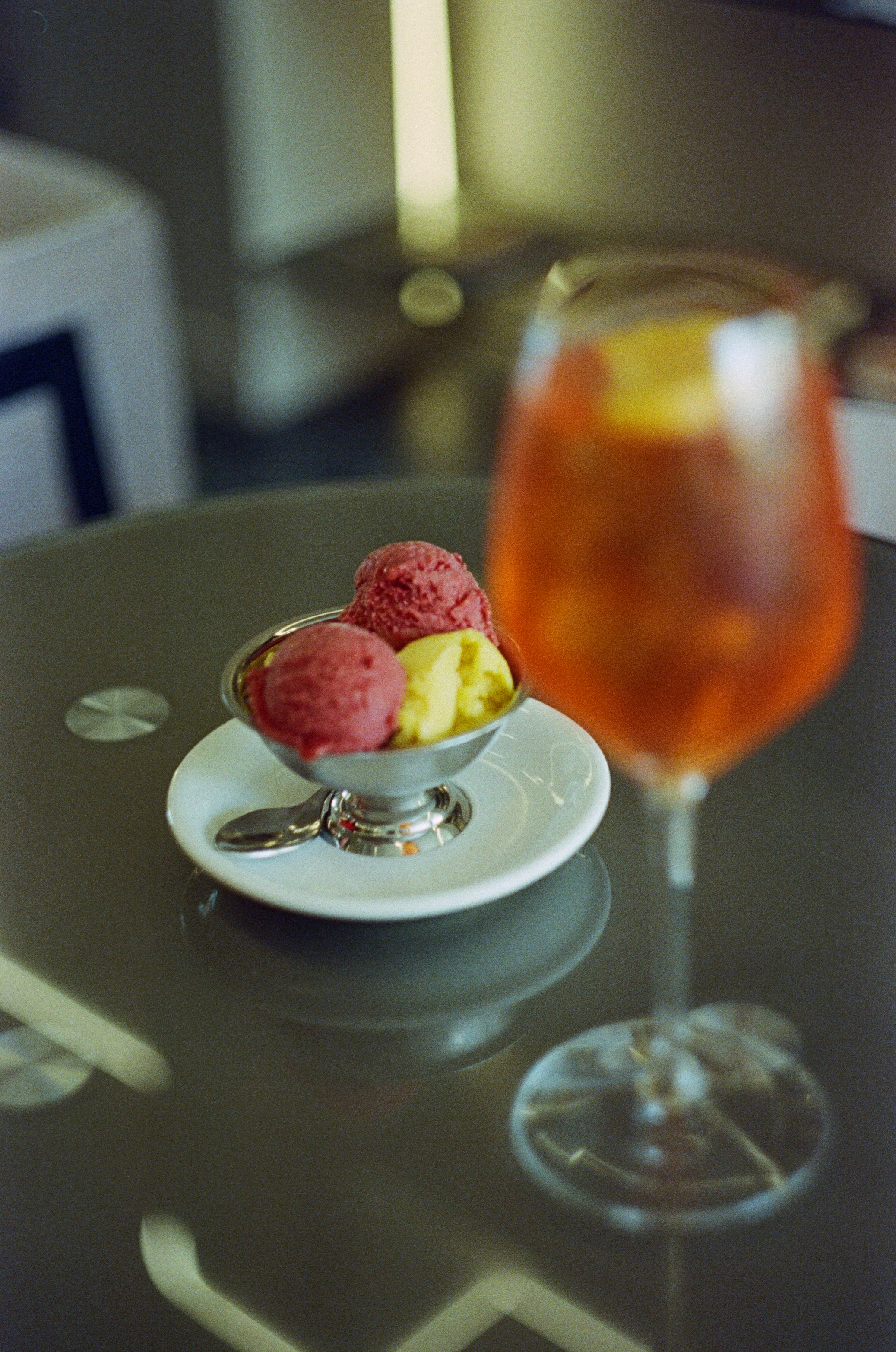 Two scoops of gelato with an orange aperitif drink.