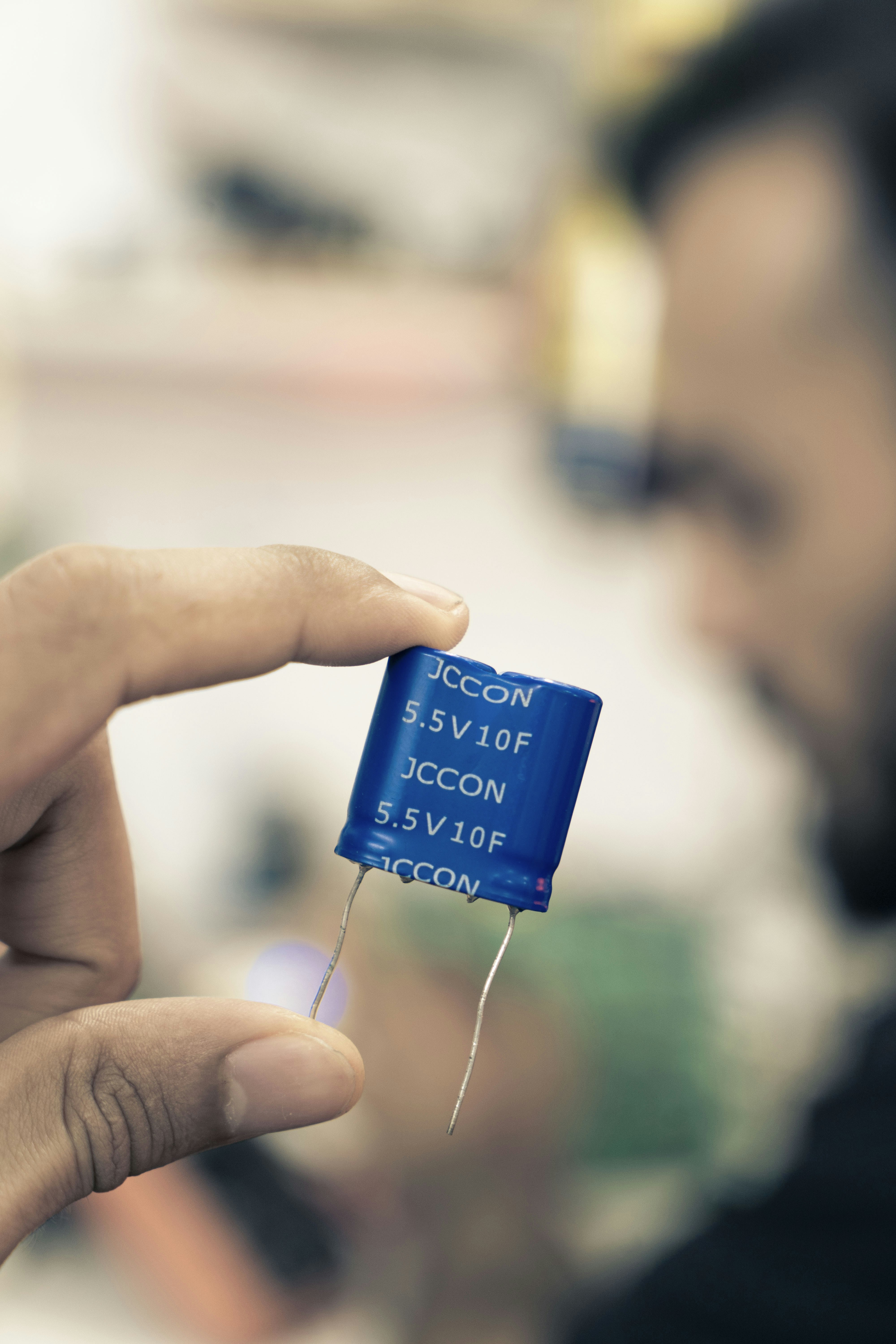 Man holding a small blue electronic capacitor