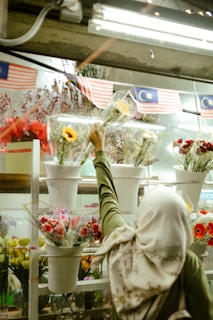 Woman in hijab selects flowers at a market.