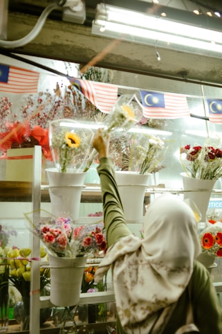 Woman in hijab selects flowers at a market.