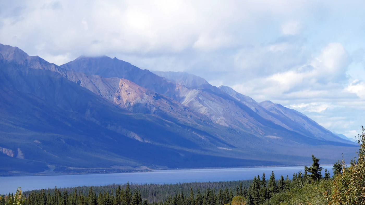Mountains reflected in a still lake in the Yukon wilderness with their mirror image perfectly doubled in the calm water below under a dramatic sky with clouds