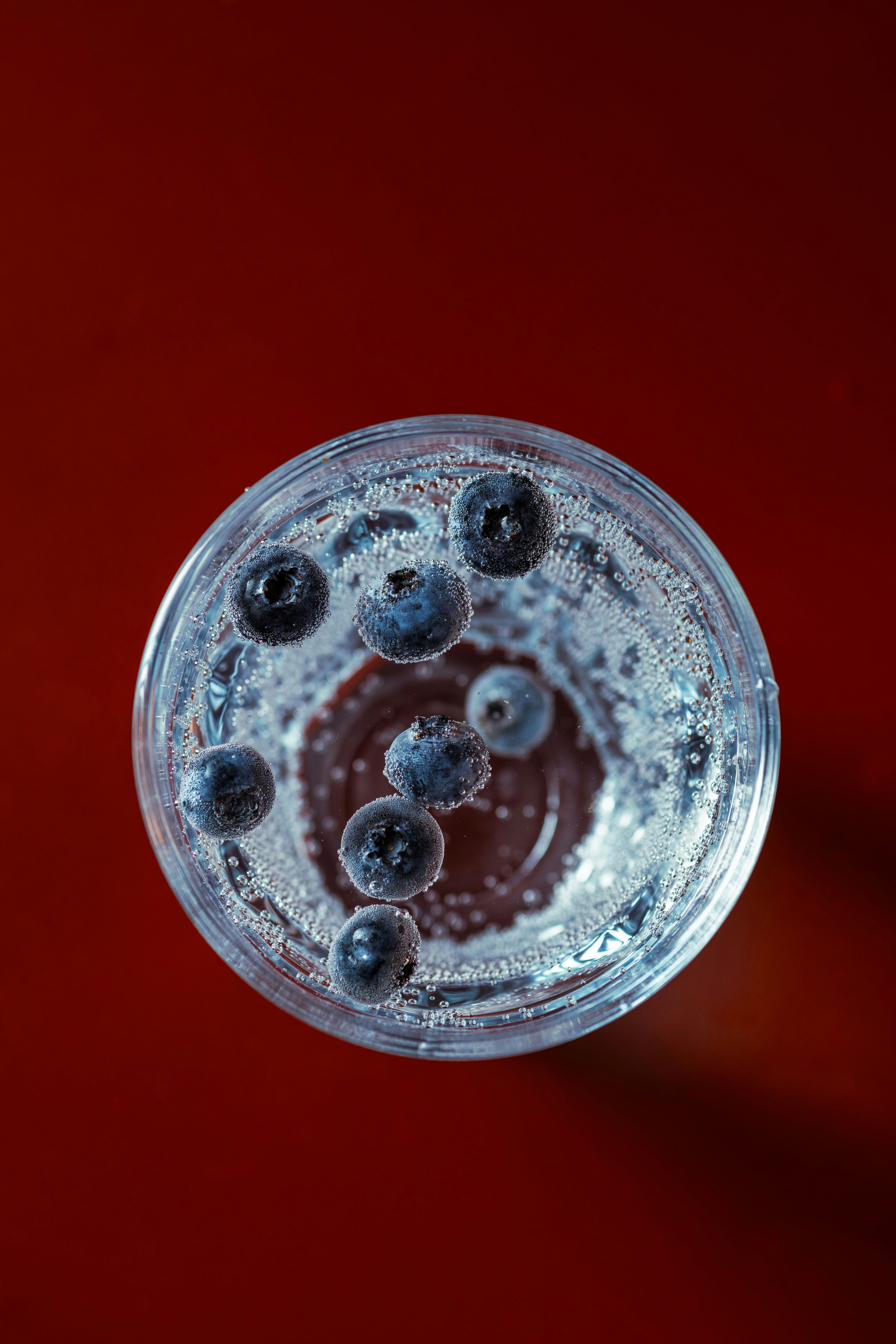 Blueberries floating in clear liquid on red background