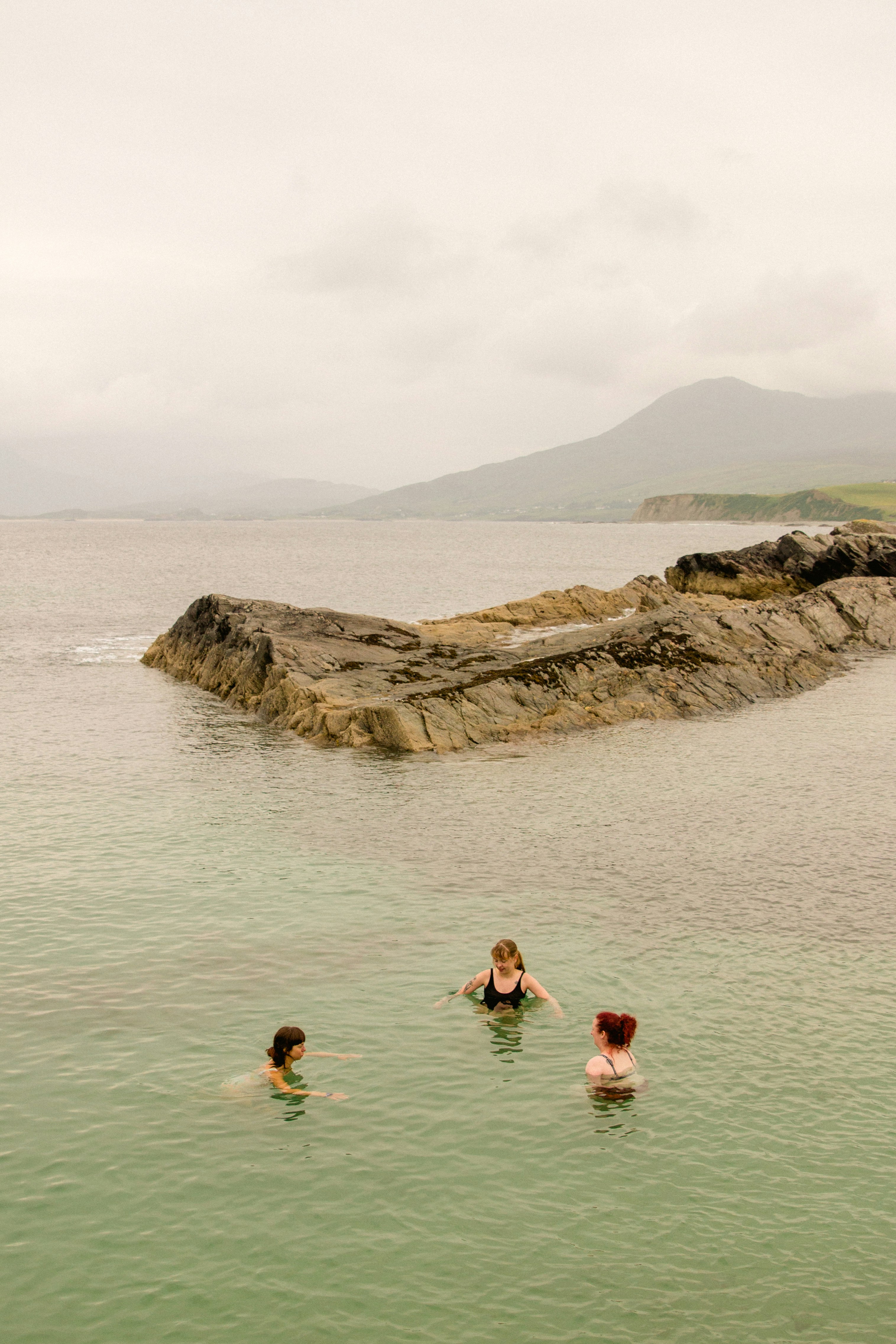 Trois personnes nageant dans une mer calme près des rochers.