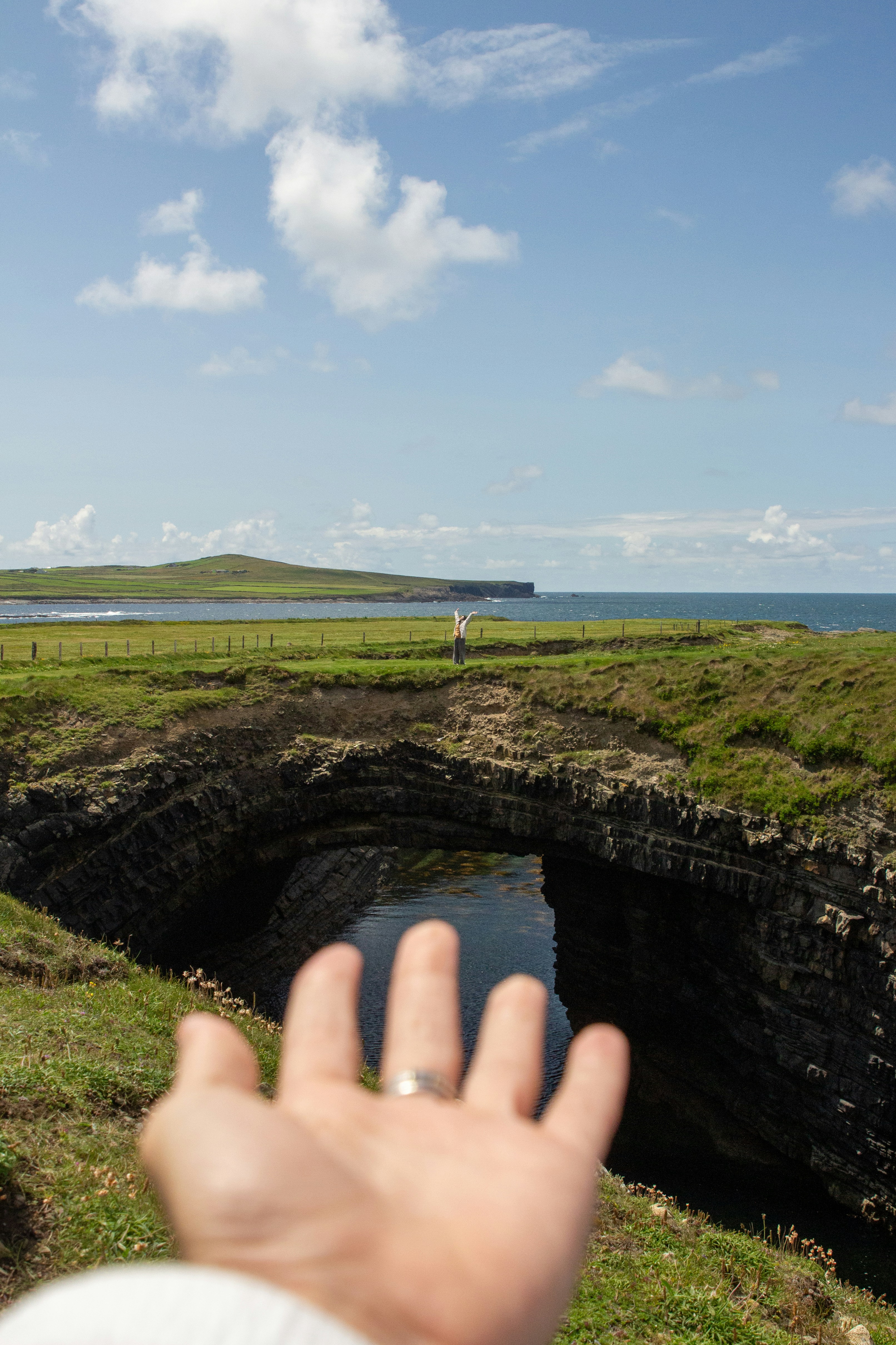 Main tendue vers une arche rocheuse naturelle au-dessus de l’eau.