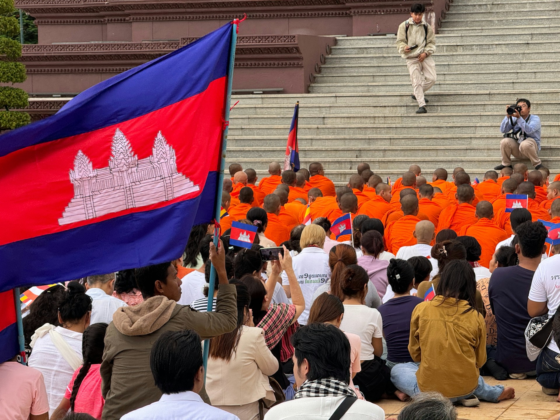 Cambodian flag with monks and people gathered outside.