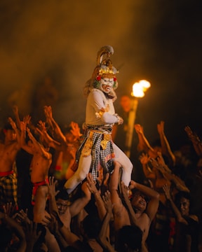 Dancer in elaborate mask carried by performers at night.