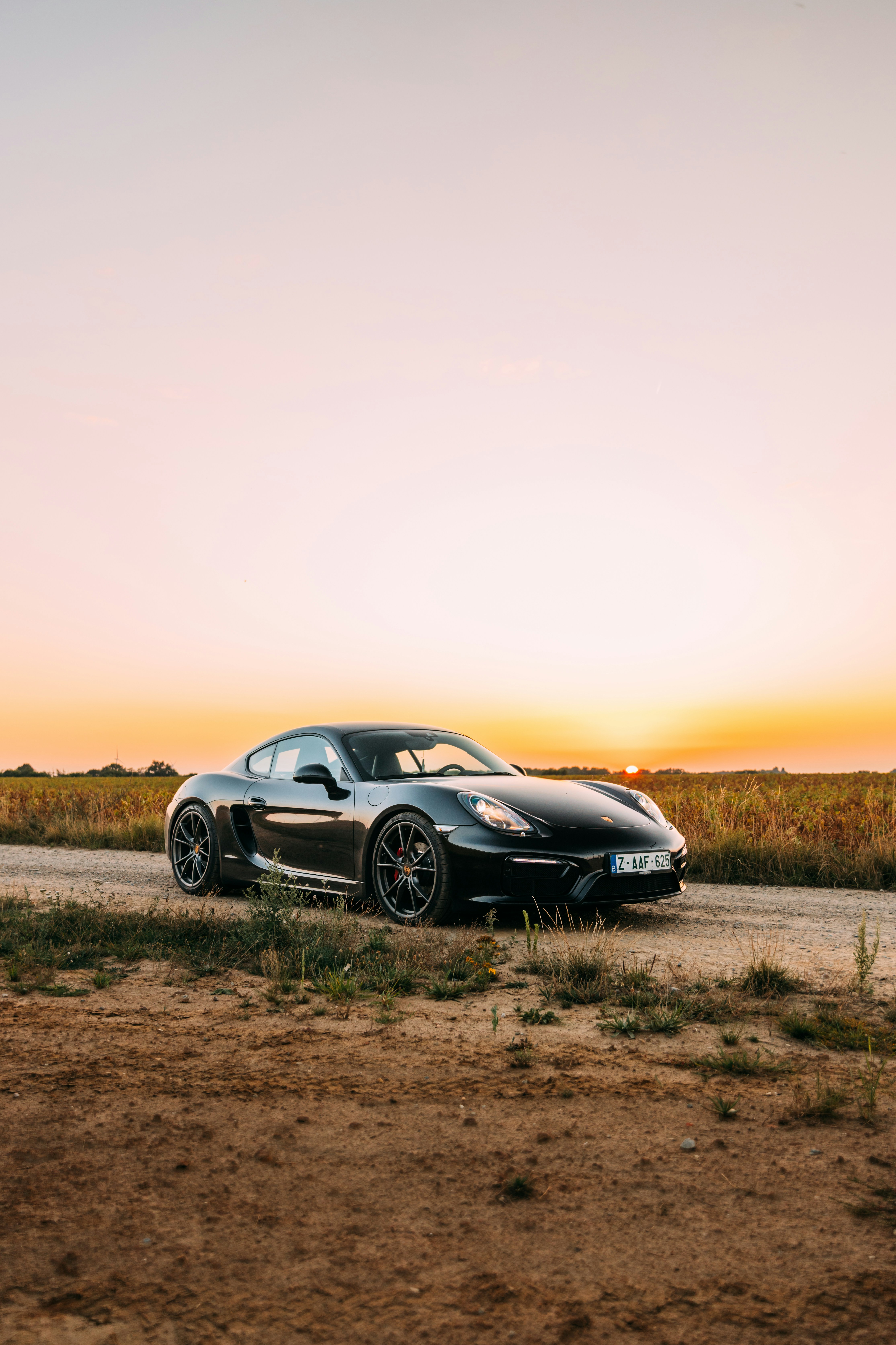 Schwarzer Sportwagen, der bei Sonnenuntergang auf einer unbefestigten Straße geparkt ist