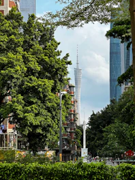 Tall tower visible between lush green trees and buildings