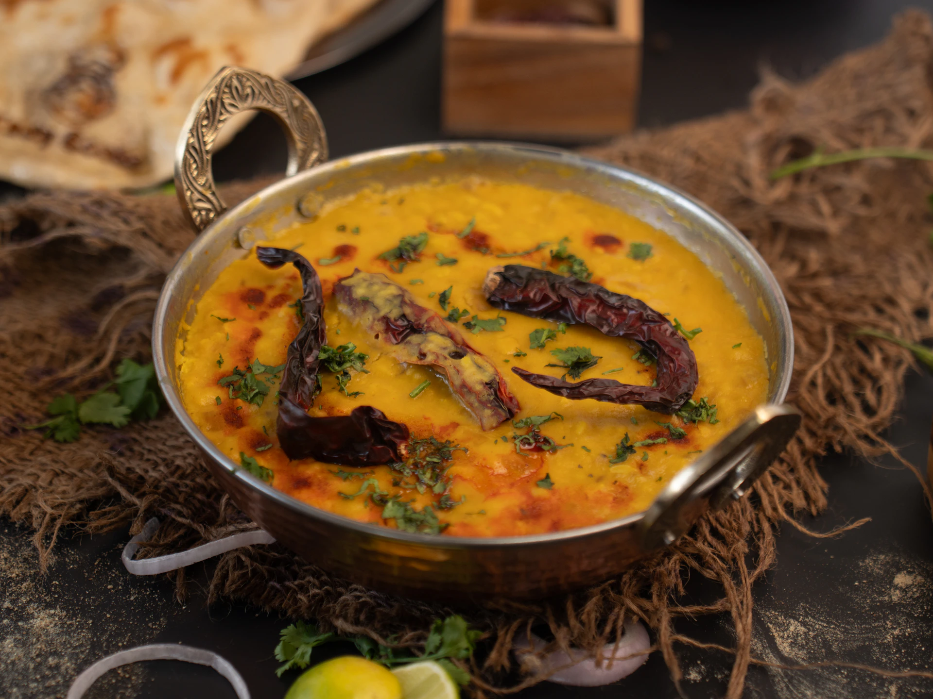 A bowl of yellow dal with garnishes and bread.