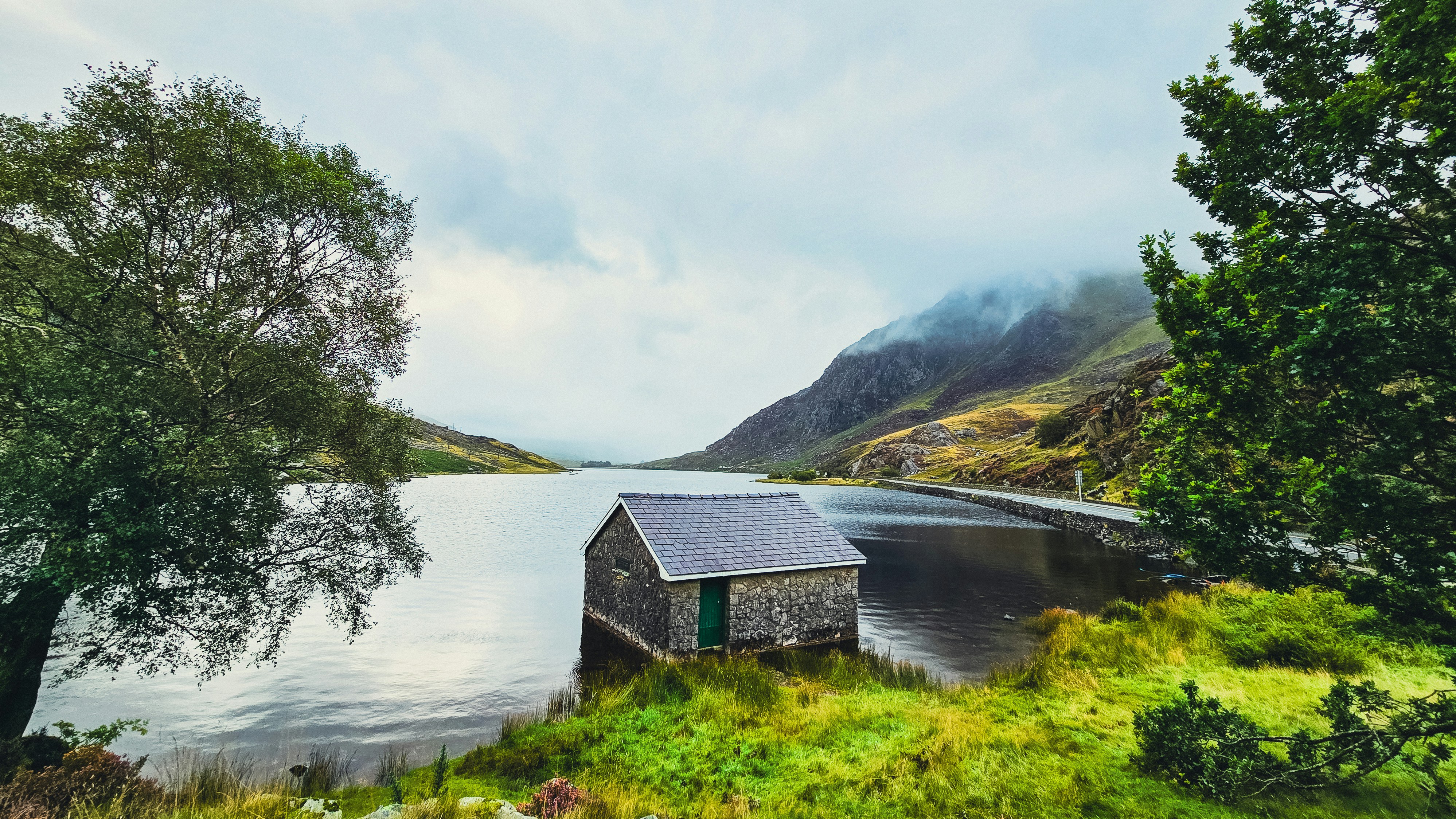 Small cabin beside a serene lake with misty mountains
