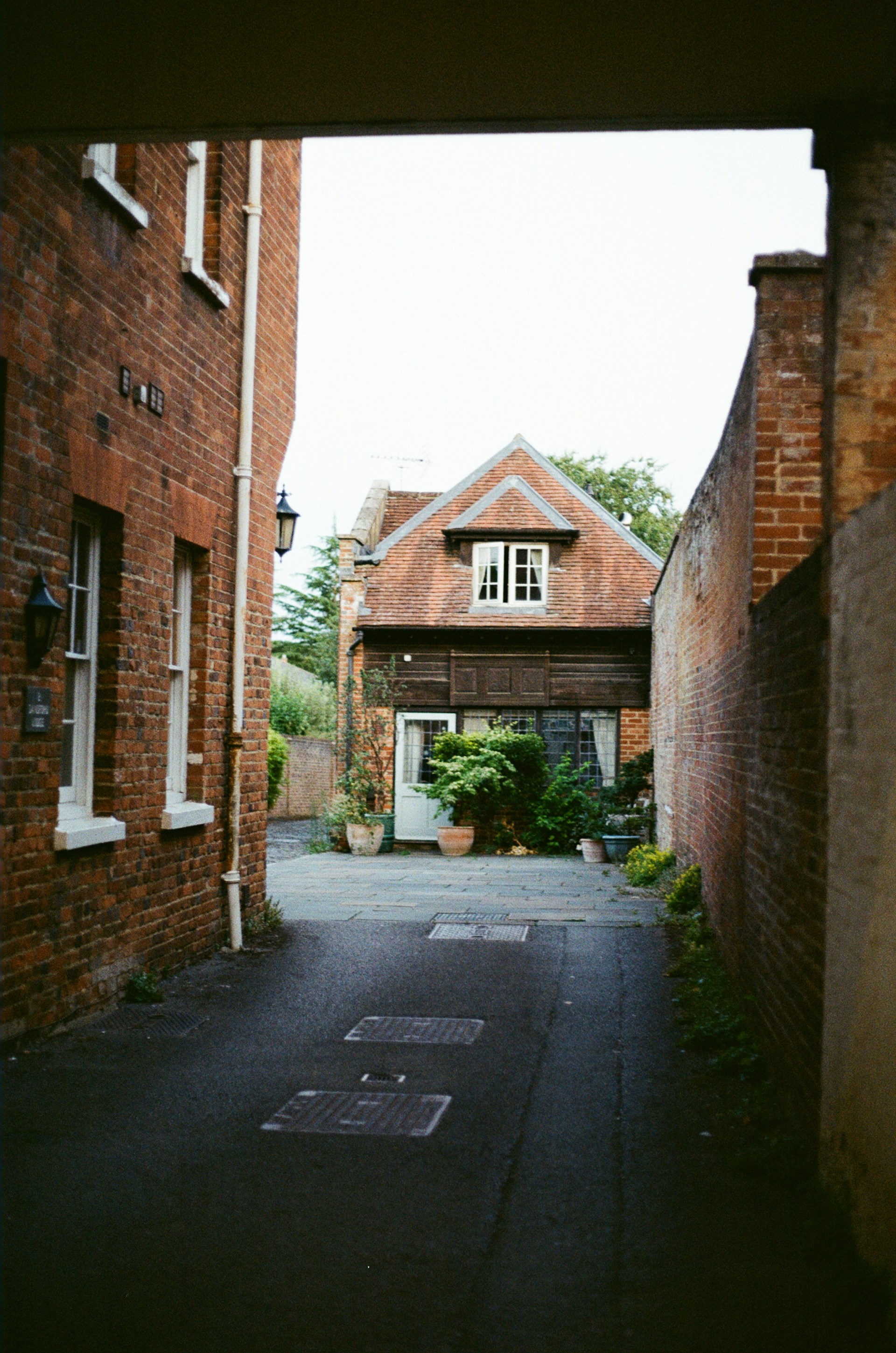 Brick buildings line a narrow alleyway leading to a house.