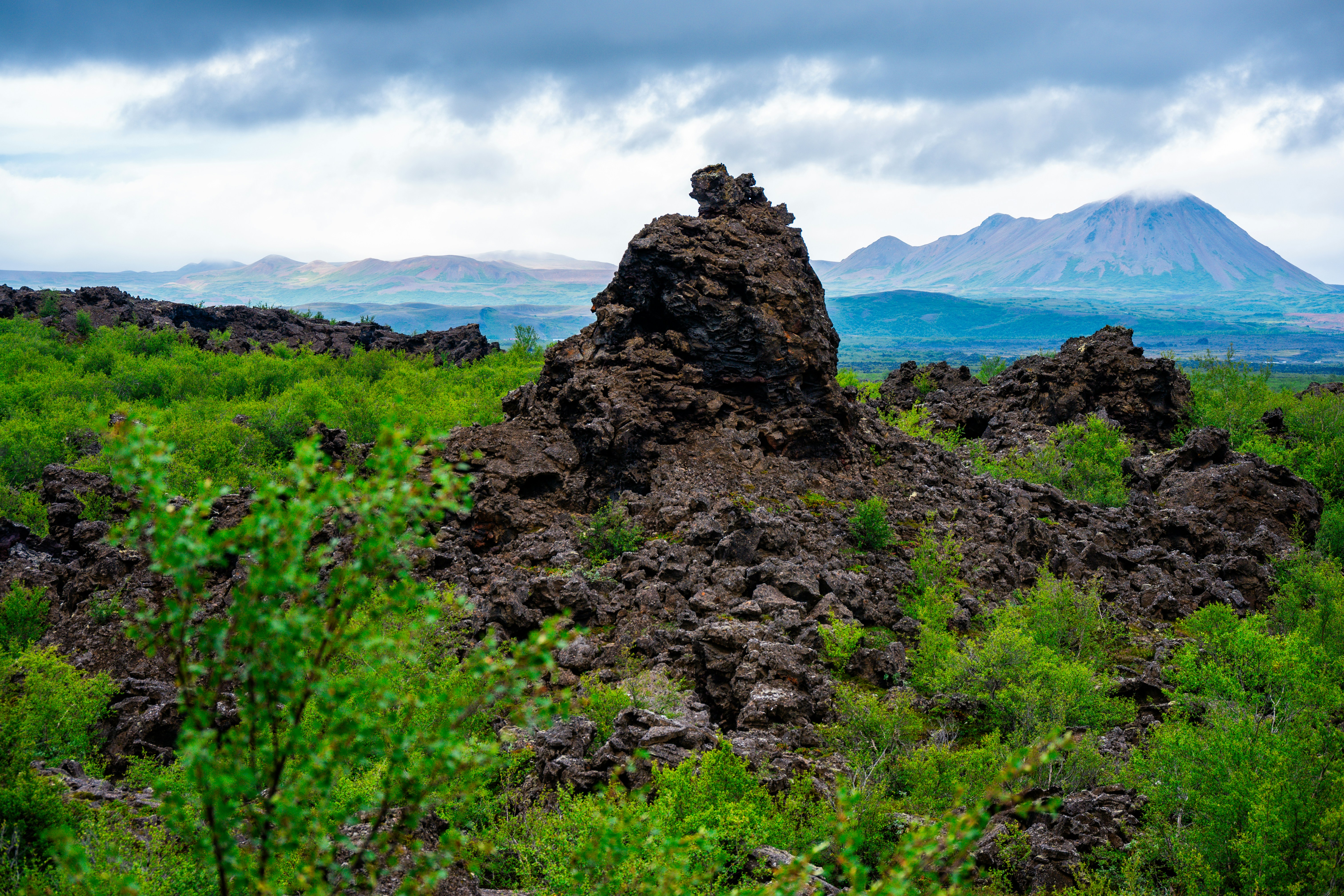 Lush green field with rocky mound and distant mountains.