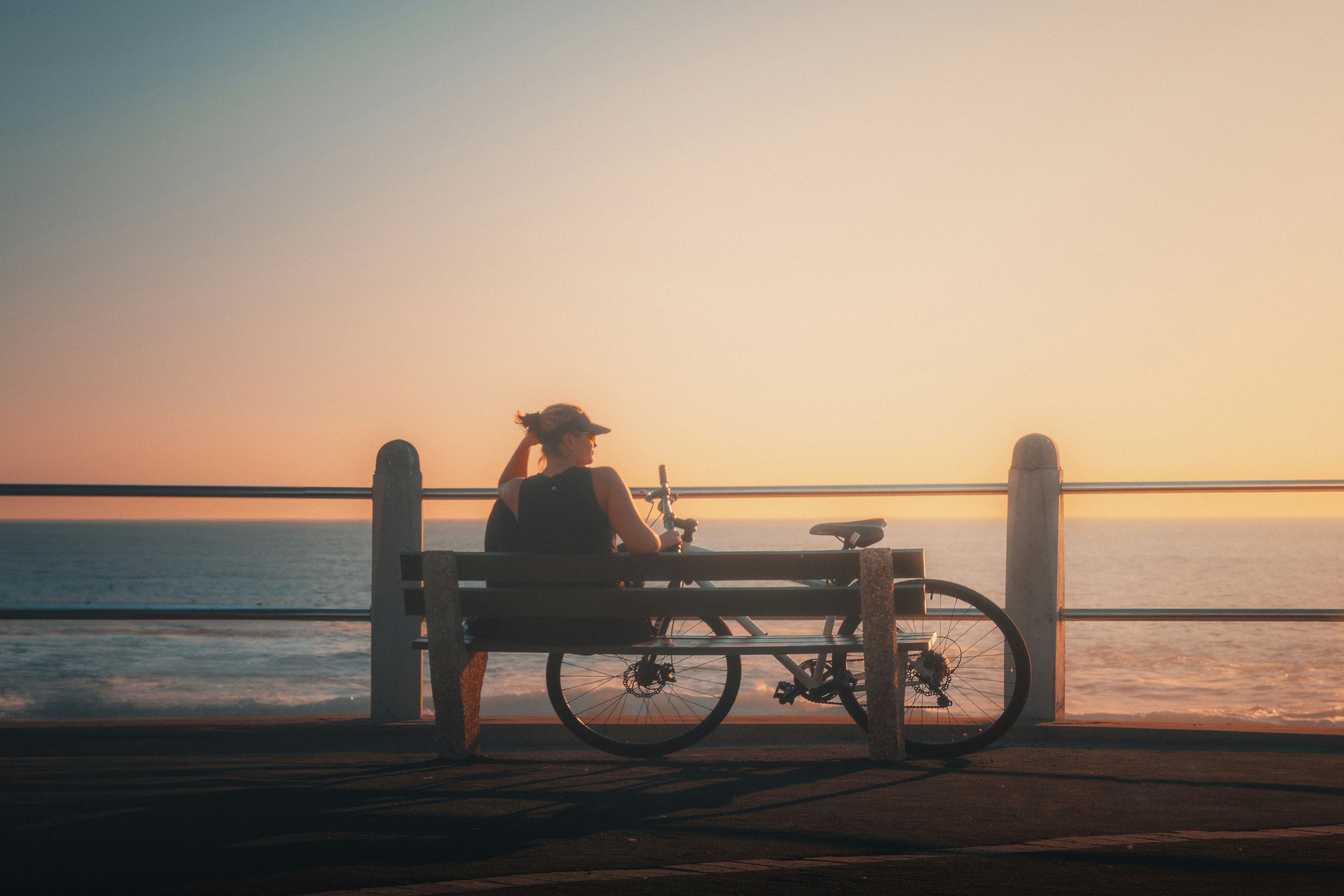 Person, die bei Sonnenuntergang auf einer Bank am Meer sitzt