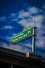 Green highway sign with directions under blue sky