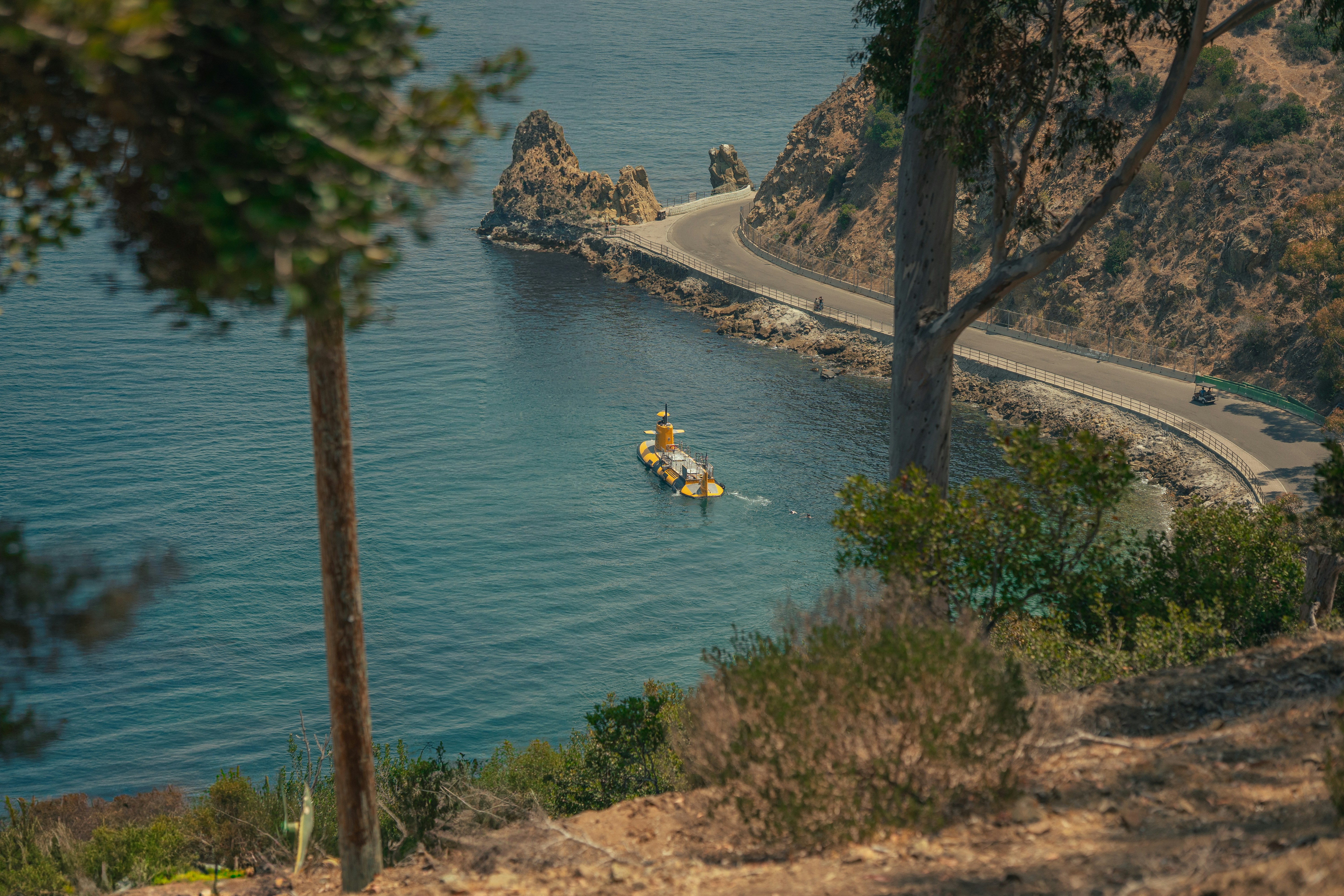 A boat floats on the calm blue water near a road.