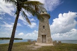 Stone lighthouse on a grassy shore with palm tree