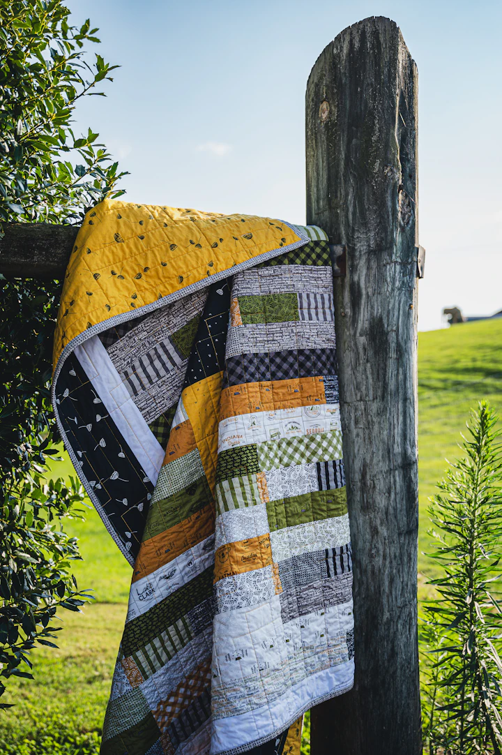 A finished patchwork quilt hung over a wooden fence post