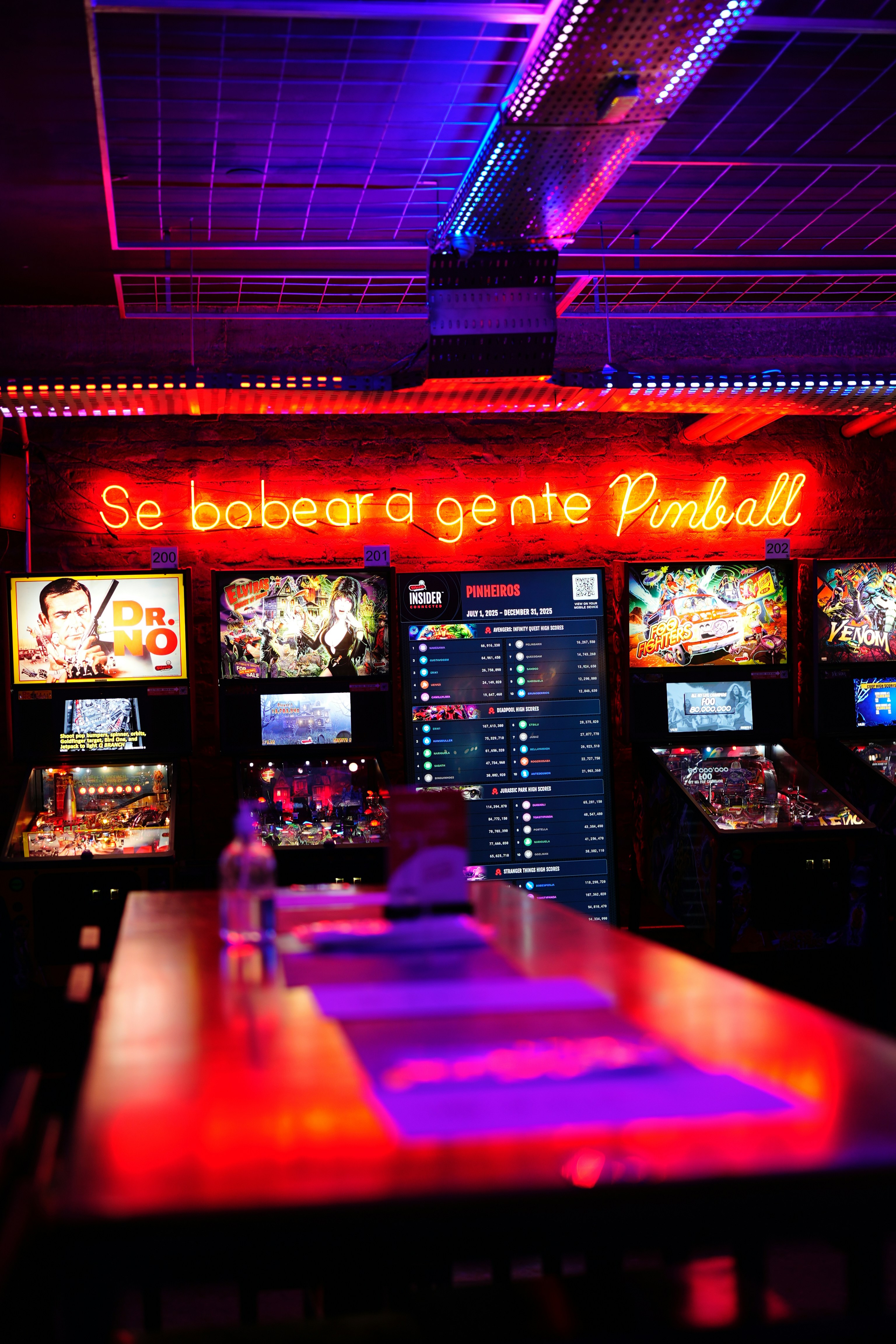 Neon signs illuminate a bar with arcade games